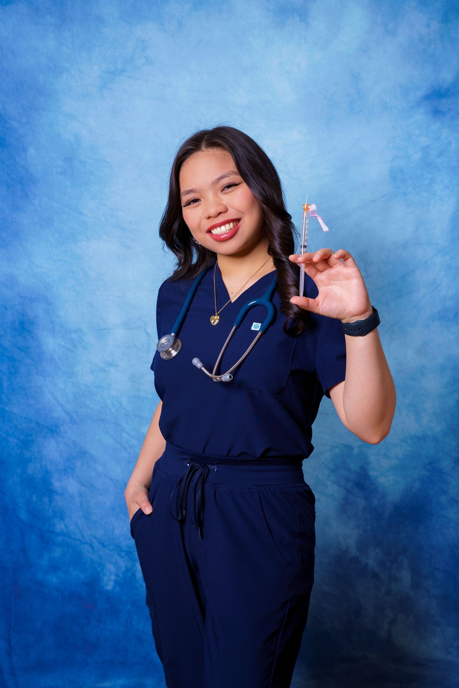 Healthcare professional in navy scrubs holds medical instrument against blue background.