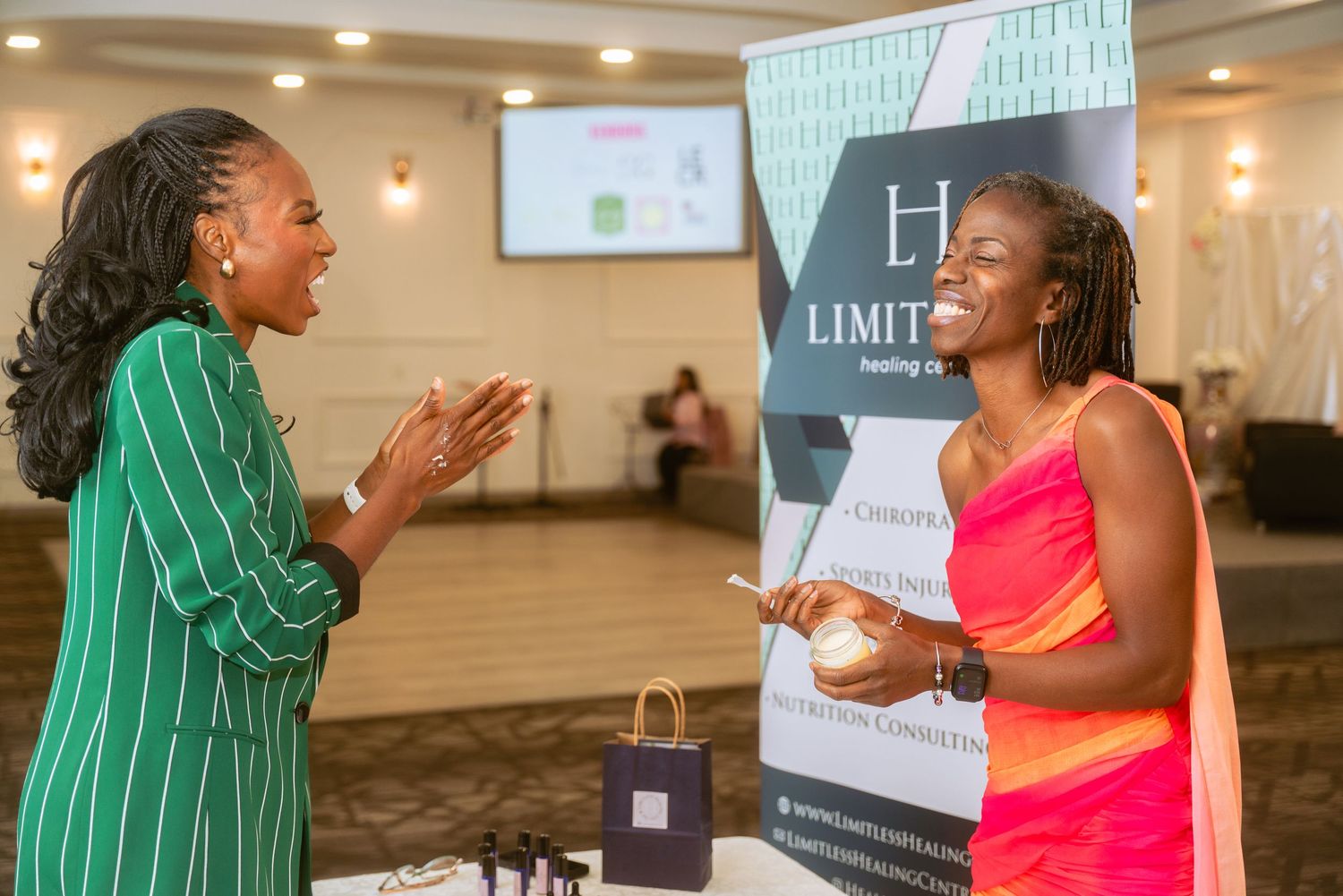 Two attendees share a joyful moment at an indoor event with bright lighting and presentation screens.
