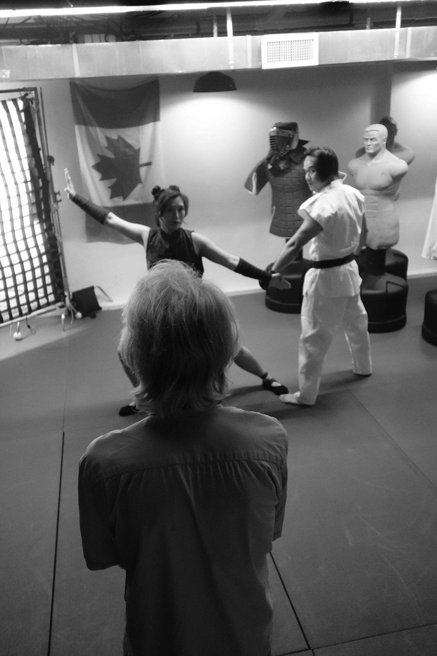 Camera operator filming martial arts students practicing in a dojo from behind.