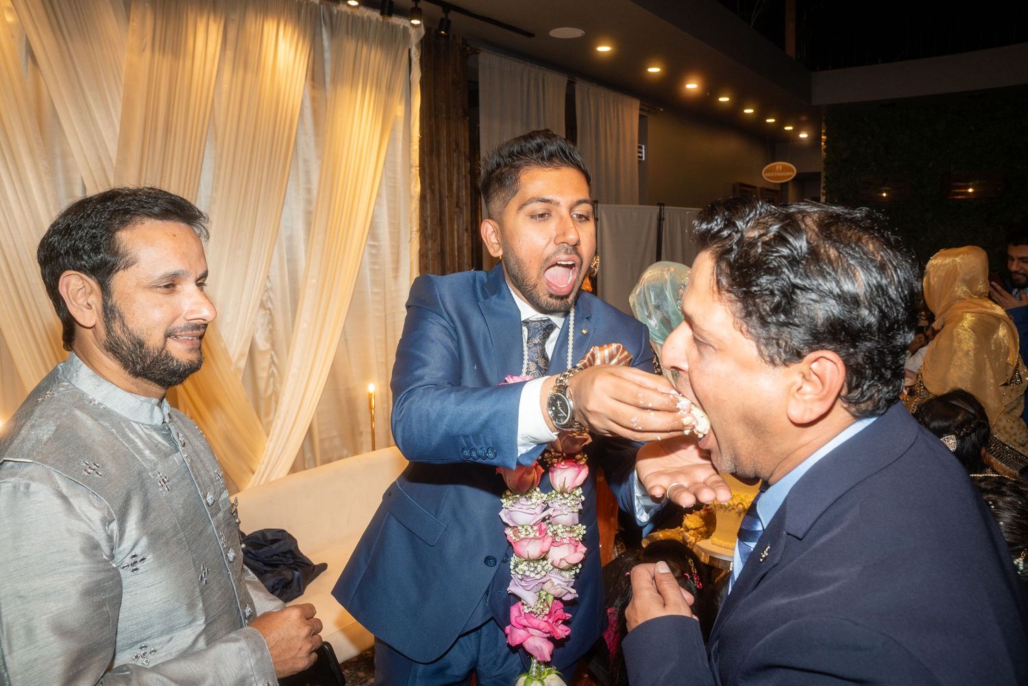 People celebrating at an evening event with warm lighting and decorative drapes.
