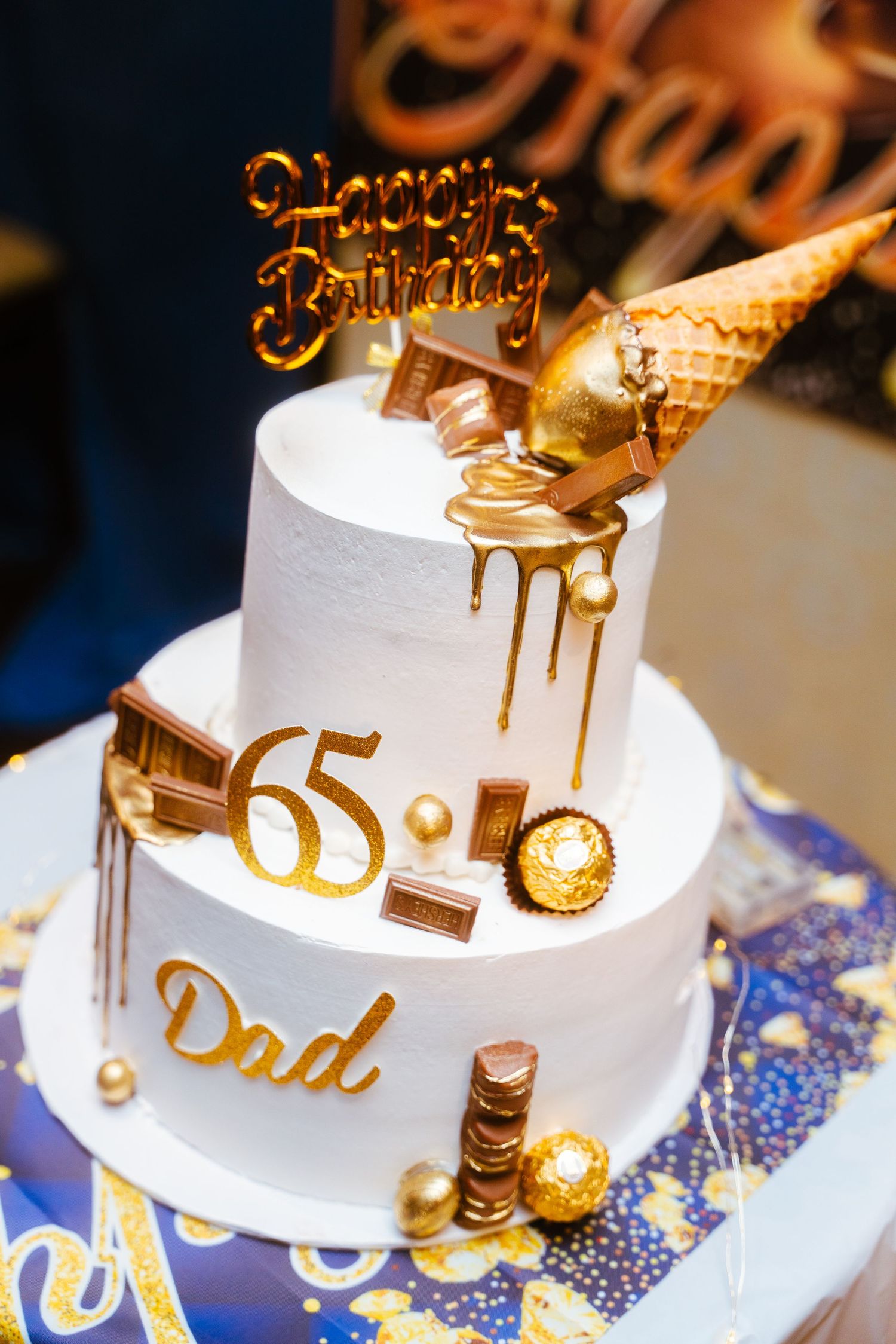 Elegant white and gold birthday cake decorated with dripping gold accents and a 65th birthday topper.