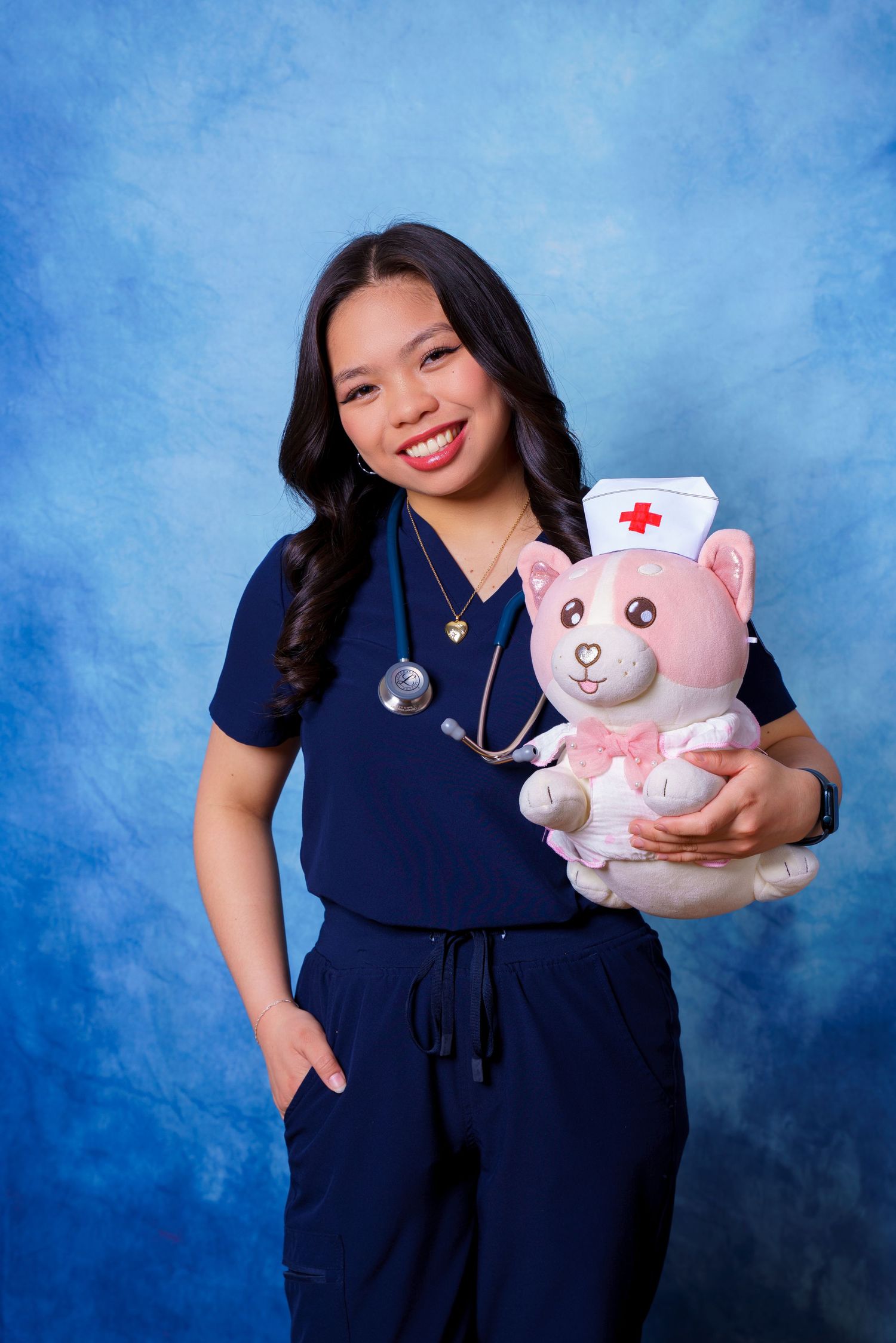 Medical professional in navy scrubs poses with pink teddy bear nurse plush toy.