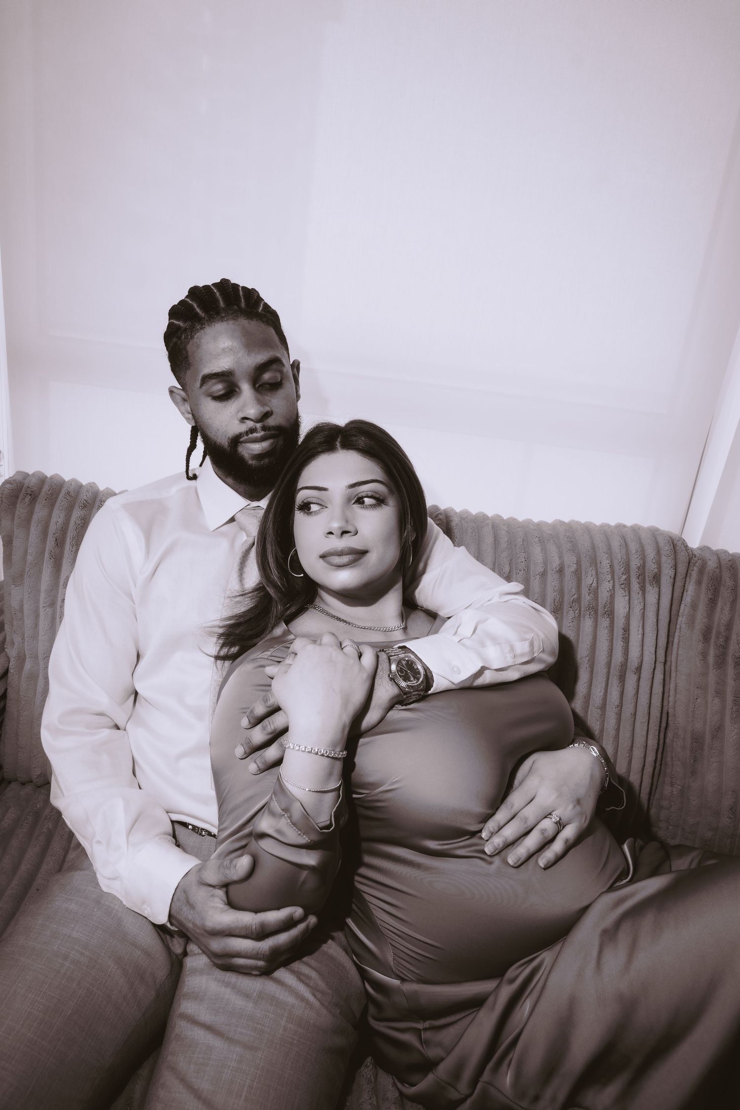 A couple relaxes together on a couch in black and white maternity photos showing tender moments of pregnancy.