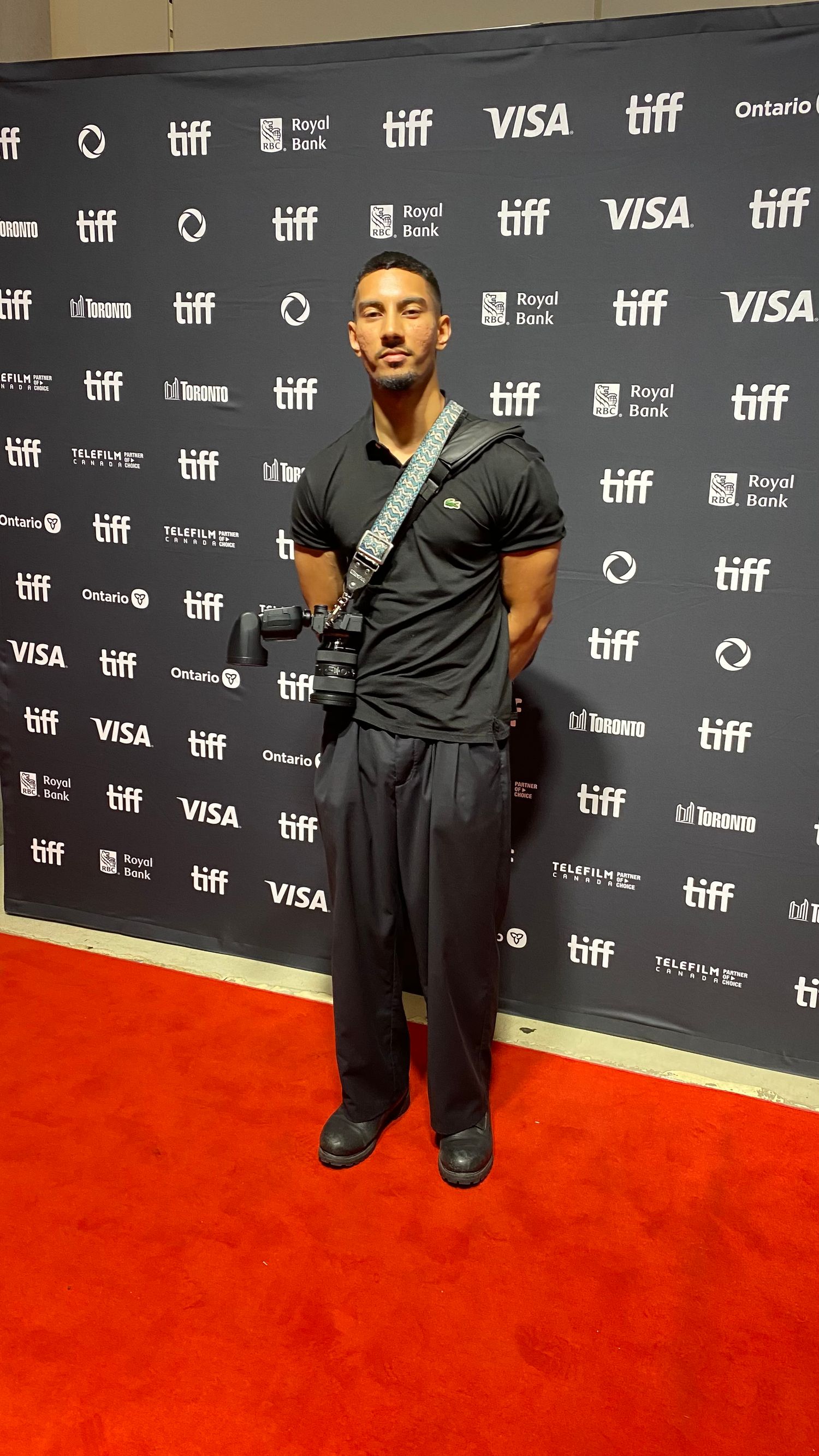 Photographer with camera strap standing on red carpet at TIFF event.