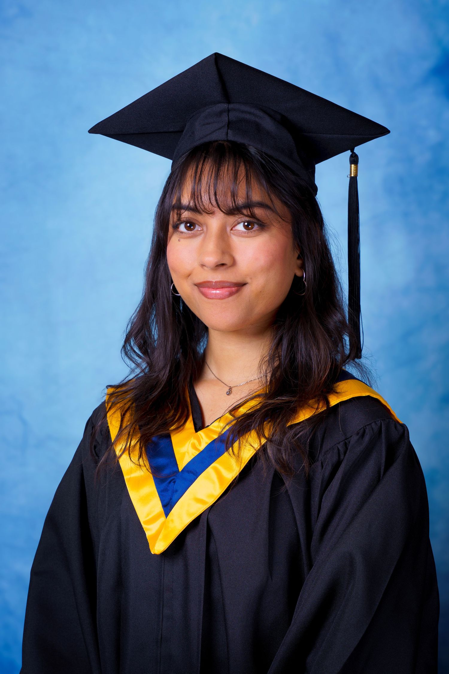 Graduate wearing mortarboard cap and black gown with gold trim poses for portraits.