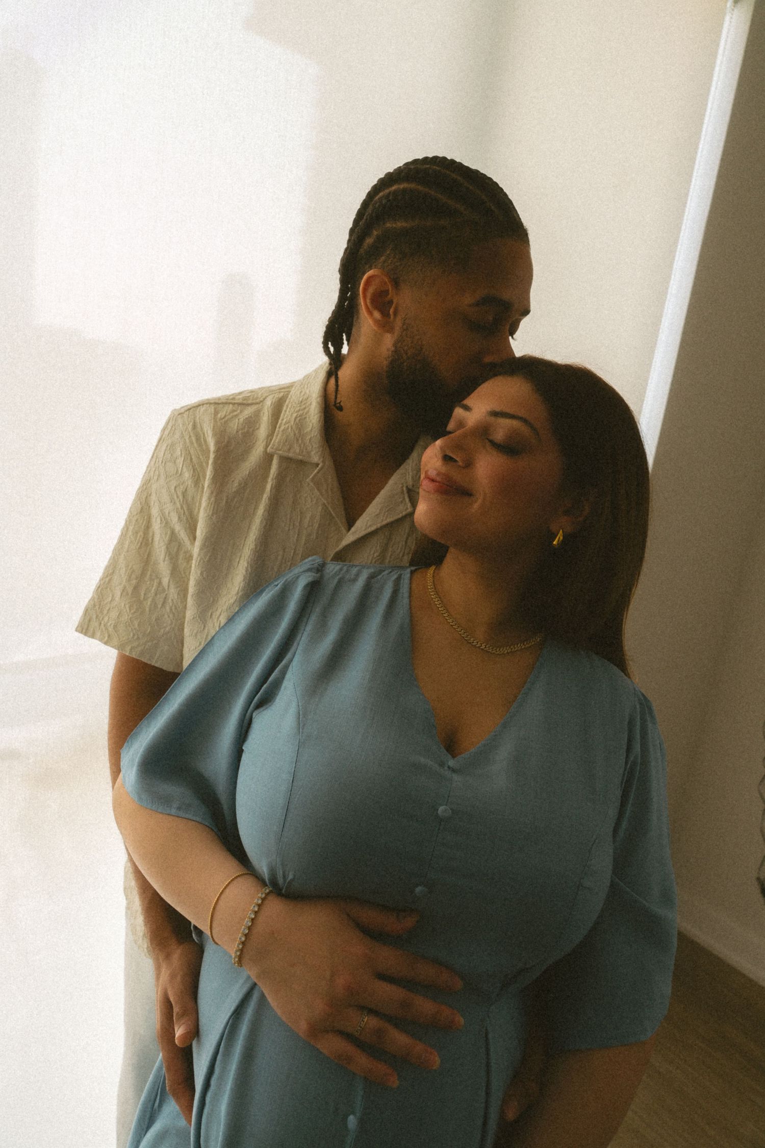 A couple embraces in a tender moment while standing in a bright room with white walls.