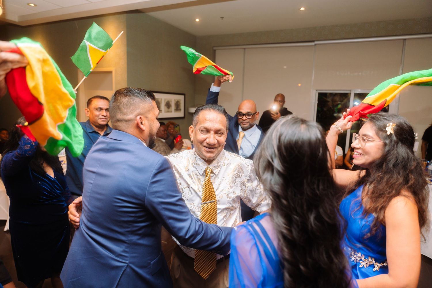 Party guests dancing and celebrating with colorful flags and decorations at a festive indoor event.