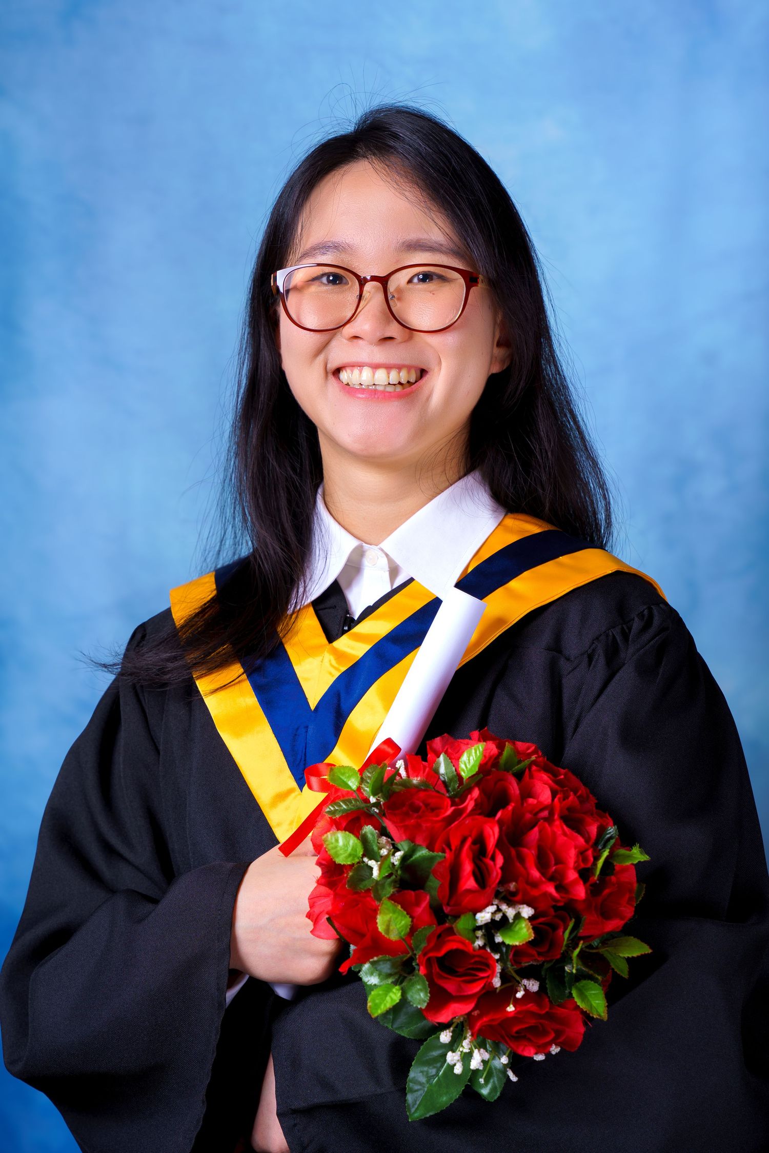 Graduate in black gown holds vibrant red roses during graduation photoshoot.