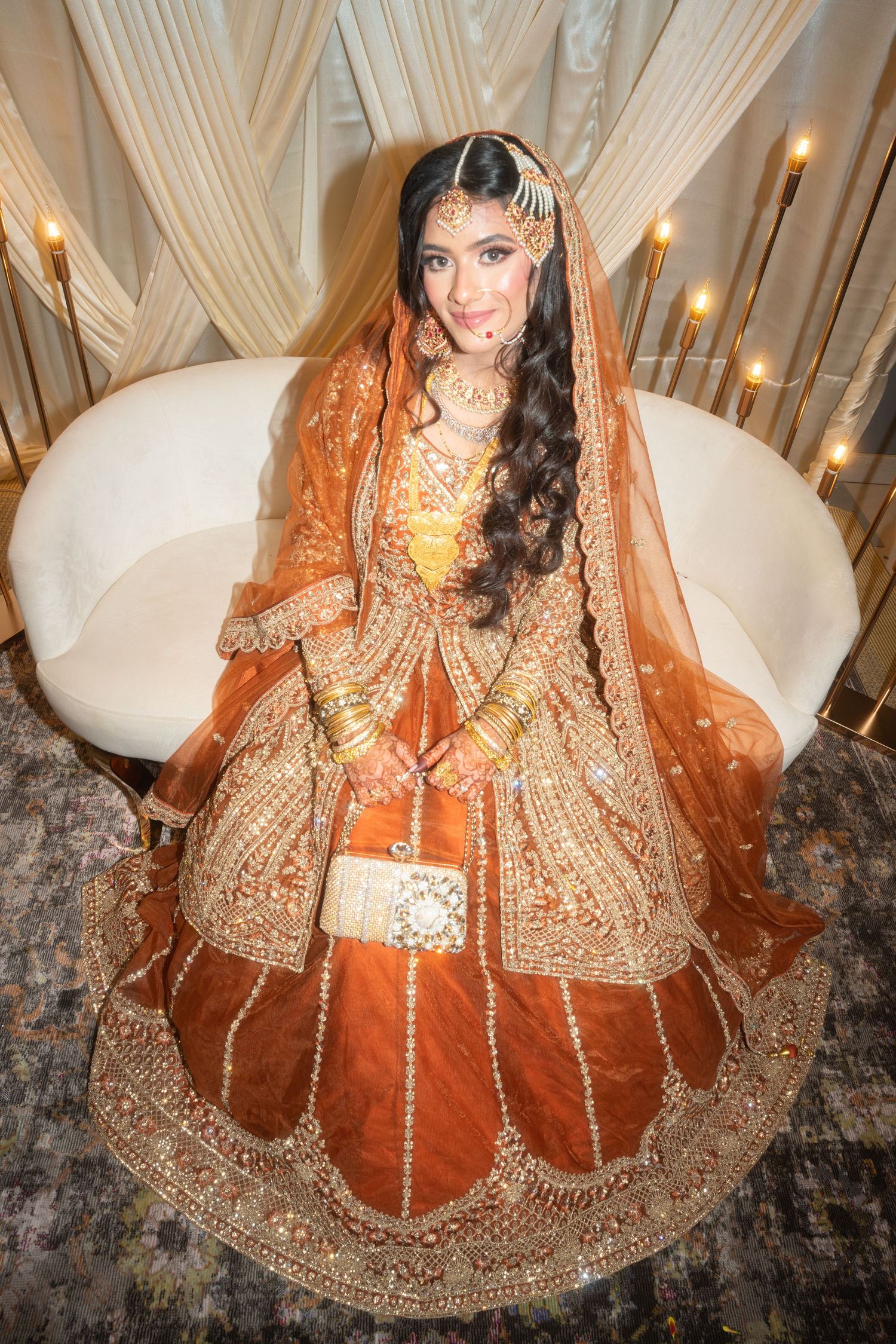 A bride in an elaborately embroidered orange and gold traditional wedding dress.