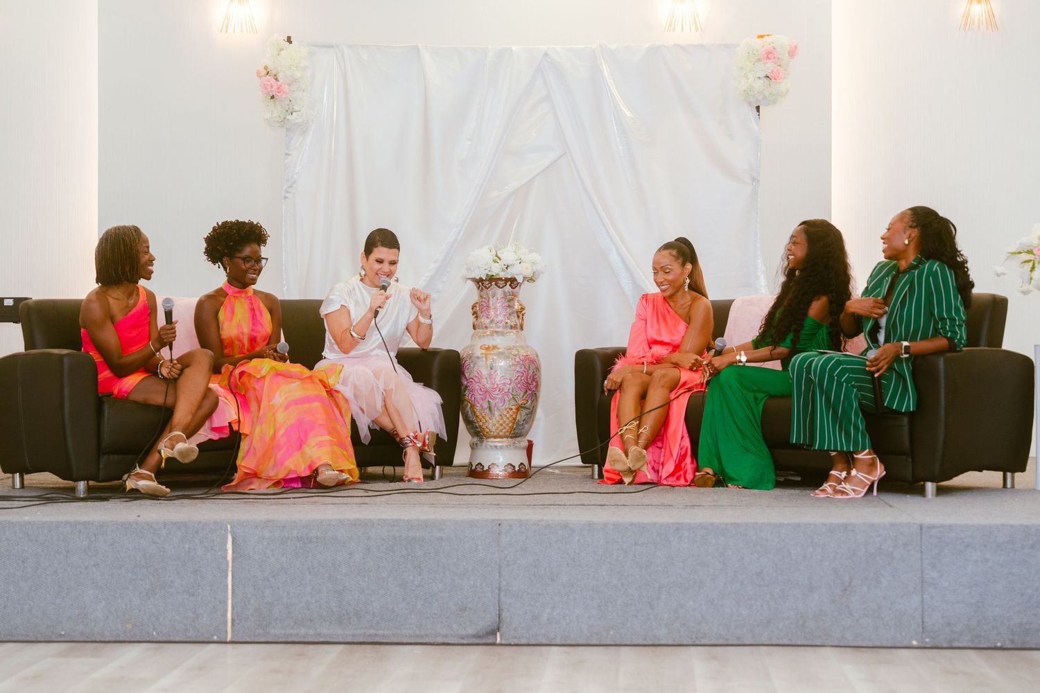 People seated on stage in bright pink and white decorated event space.