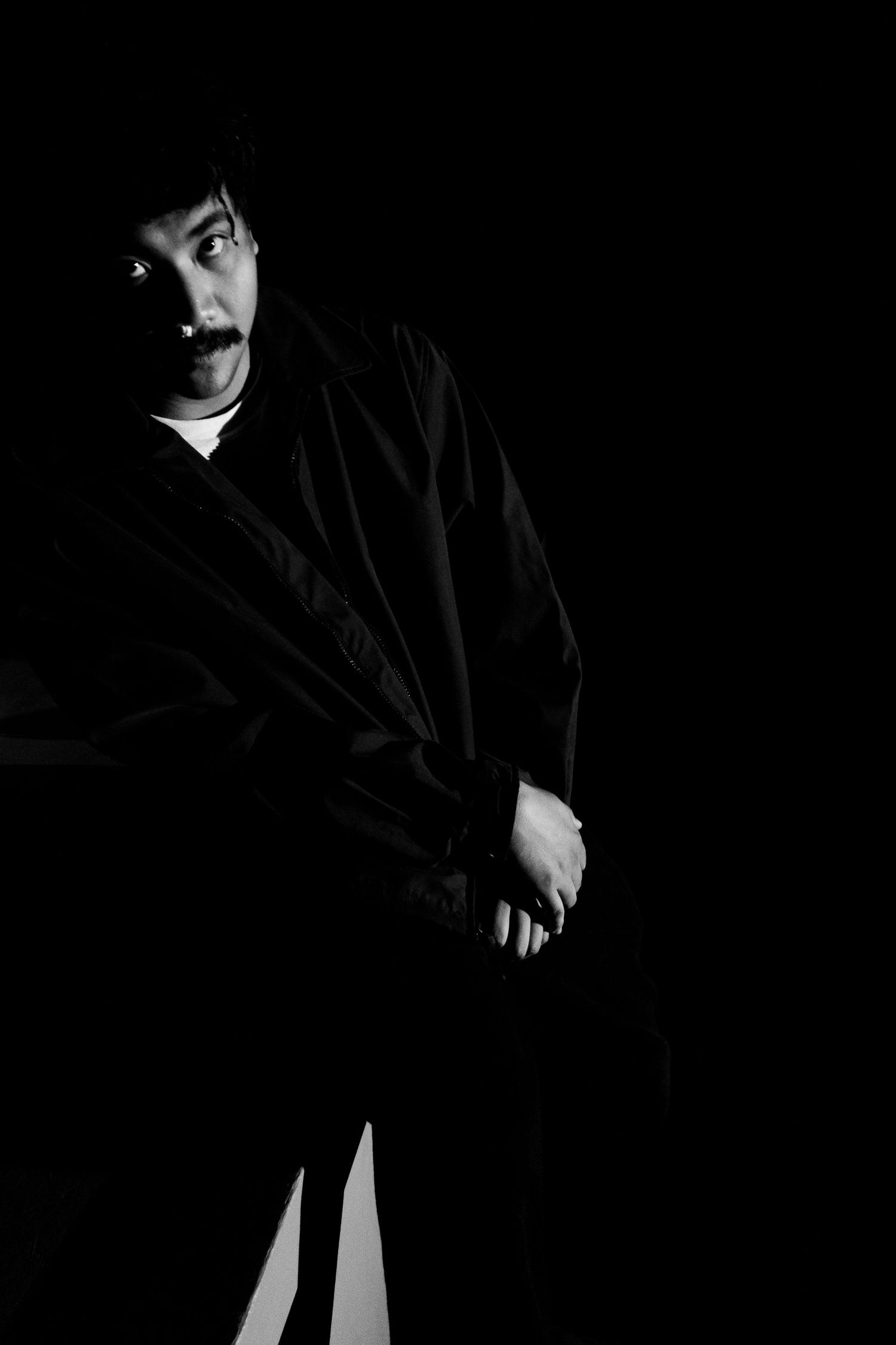 Dramatic black and white portrait of someone in dark clothing against black background.