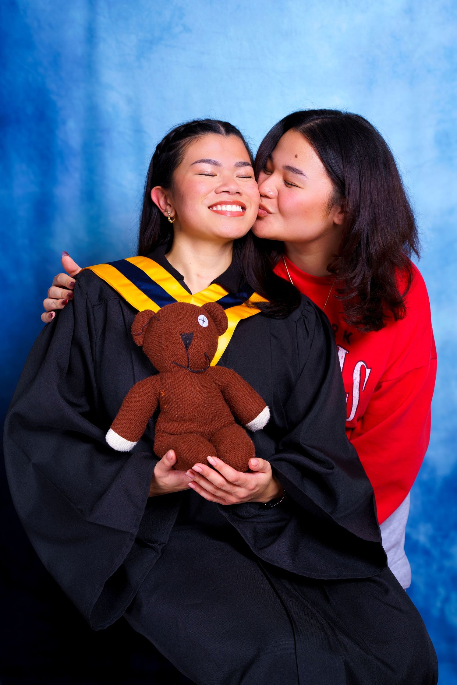 Graduation portrait featuring graduate in academic regalia holding brown teddy bear.