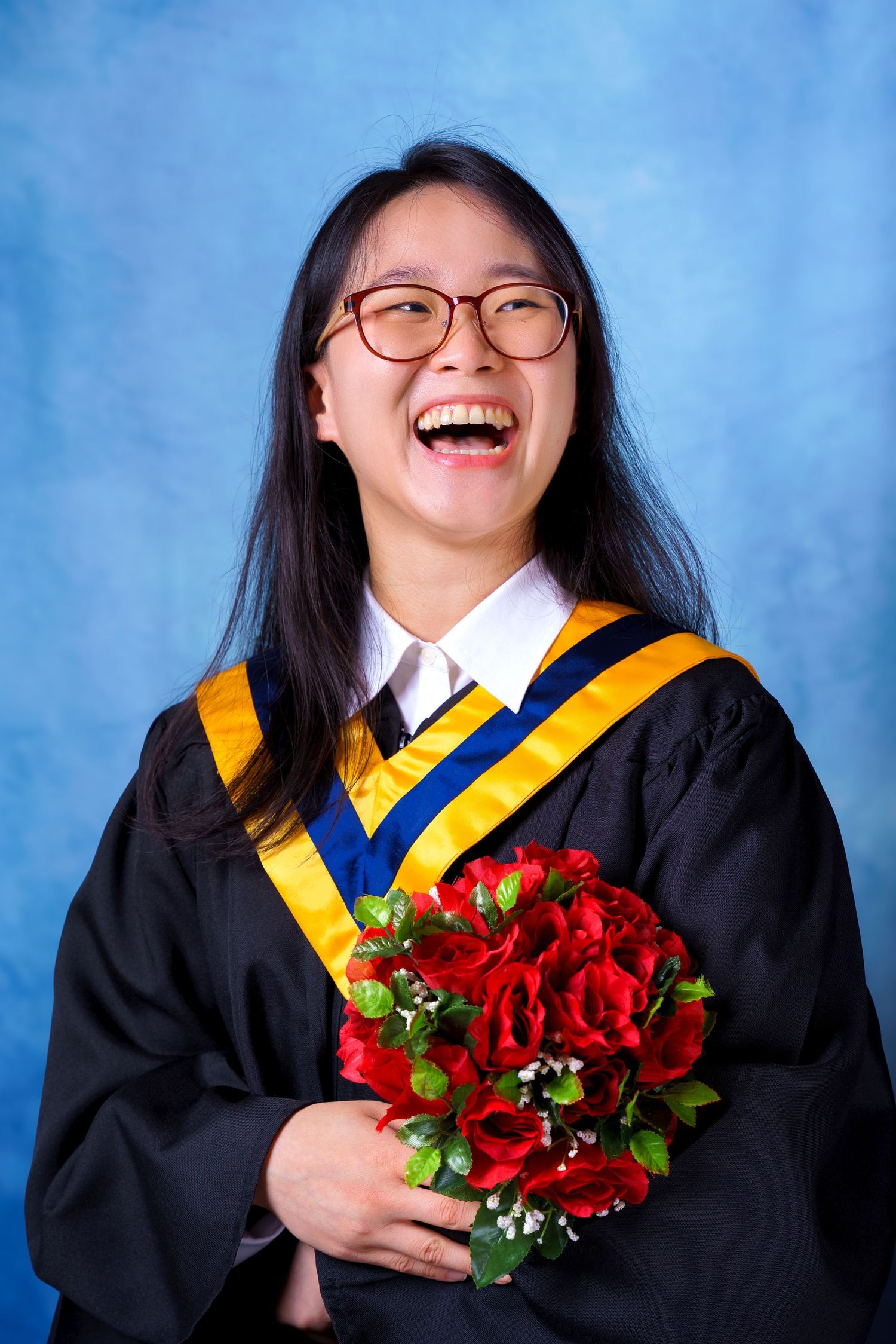 Graduate with glasses displays joyful expression while holding red roses.