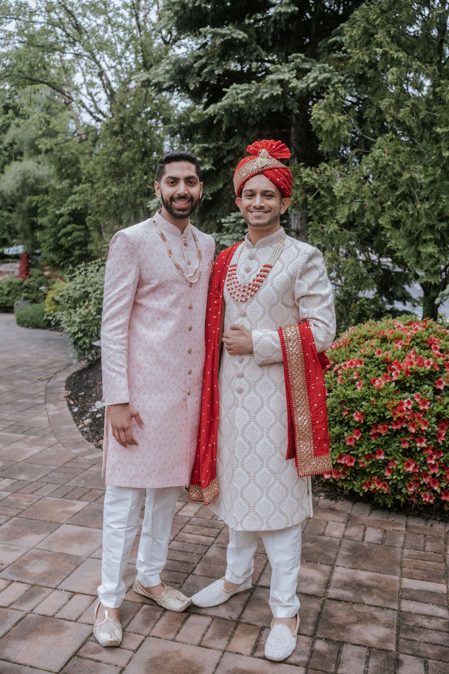 Two grooms in traditional Indian sherwanis posing together outdoors at a South Asian wedding celebration.