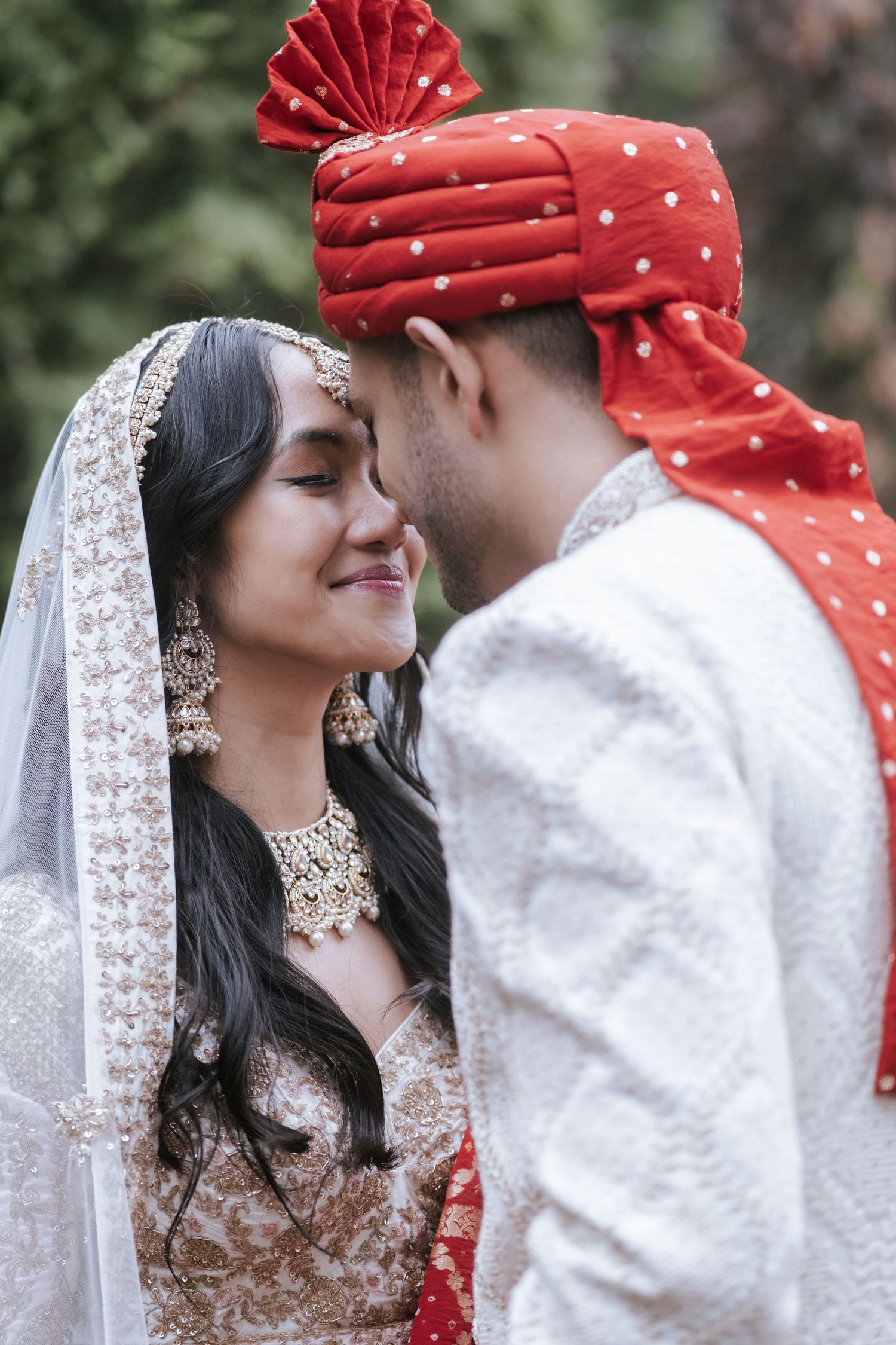 Intimate moment between Indian bride and groom touching foreheads during outdoor wedding portrait in traditional attire.