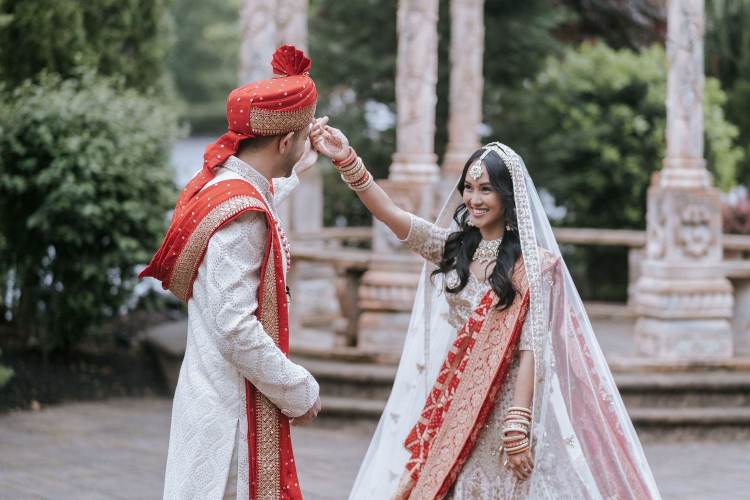 Indian groom twirling his smiling bride in white lehenga and red dupatta during outdoor wedding portraits.