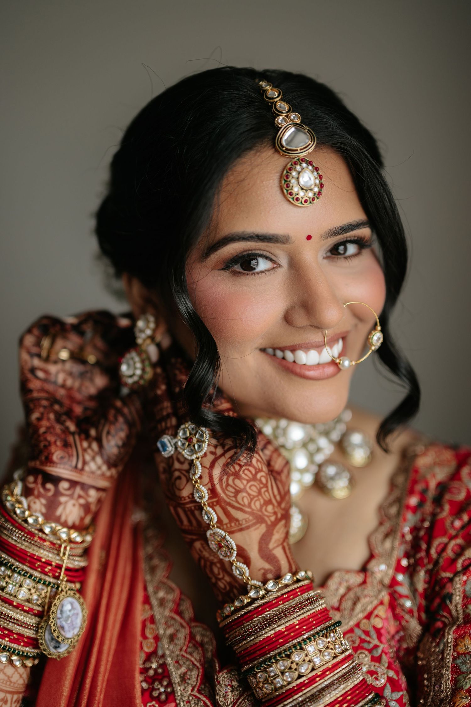 Beautiful Indian bride smiling in red bridal lehenga with kundan jewelry and mehndi hands.