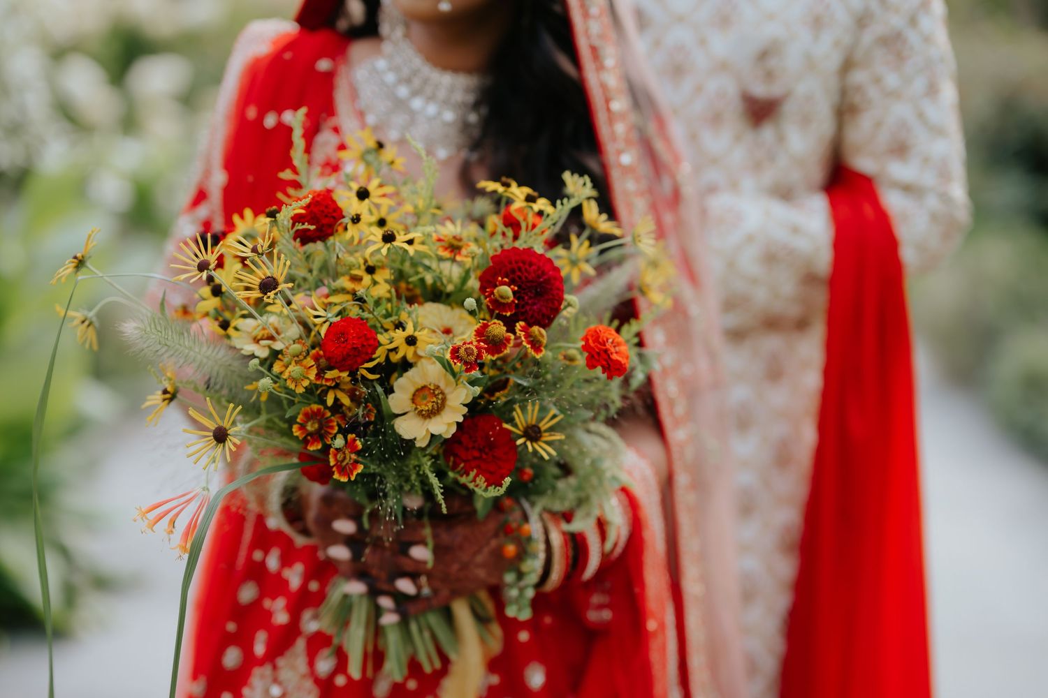 Close-up of Indian bride holding vibrant red and yellow wedding bouquet in red lehenga with mehndi.