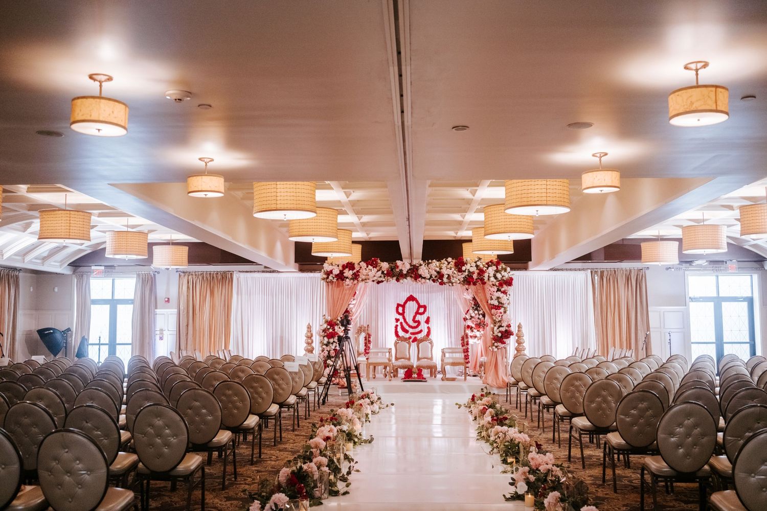 Indian wedding ceremony hall with white chairs, floral aisle, and a decorative Ganesha mandap altar.