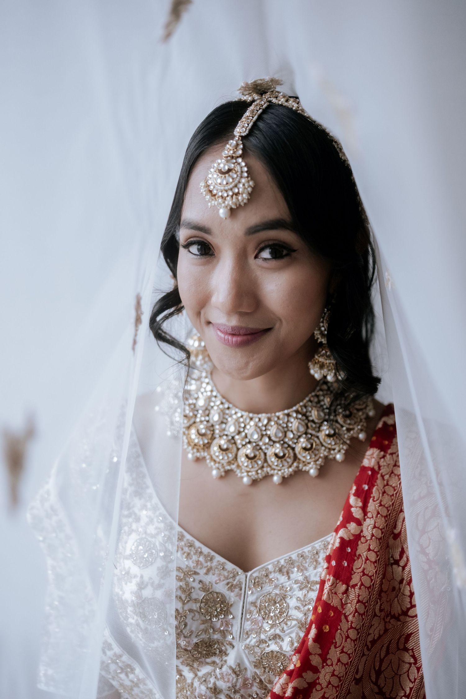 Beautiful Indian bride wearing ornate gold kundan necklace, maang tikka, and white embroidered lehenga with veil.