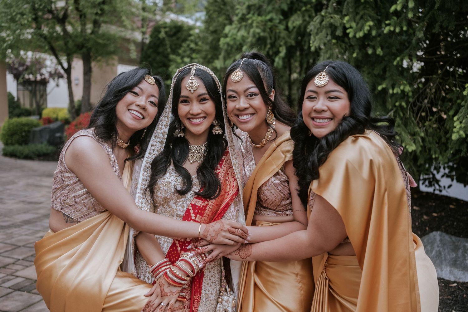 Bride in red and gold Indian bridal attire posing joyfully with three bridesmaids in gold sarees.