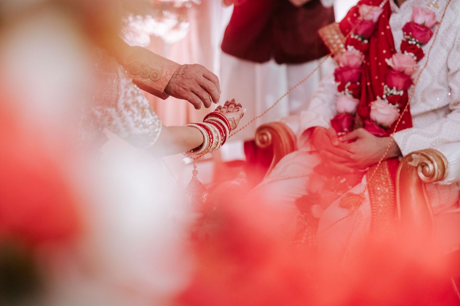 Close-up of bride's henna-adorned hands with red bangles during Hindu wedding ritual.