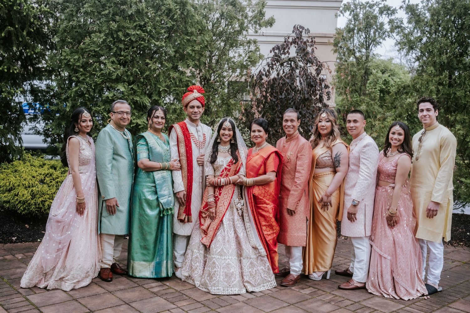 Indian wedding family portrait with bride, groom, and relatives dressed in colorful traditional attire outdoors.
