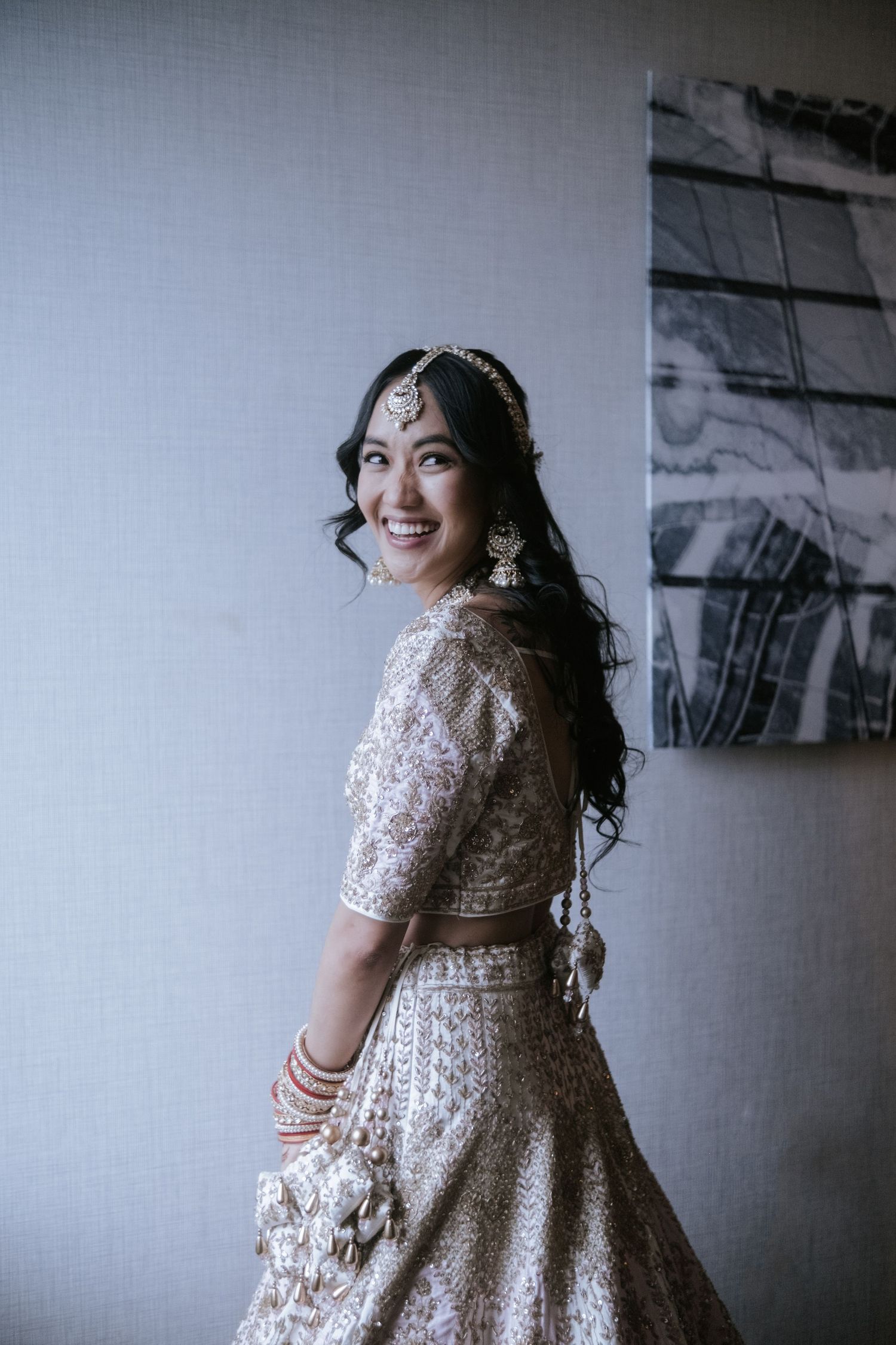 Beautiful Indian bride in ornate gold lehenga and traditional jewelry smiles over shoulder.
