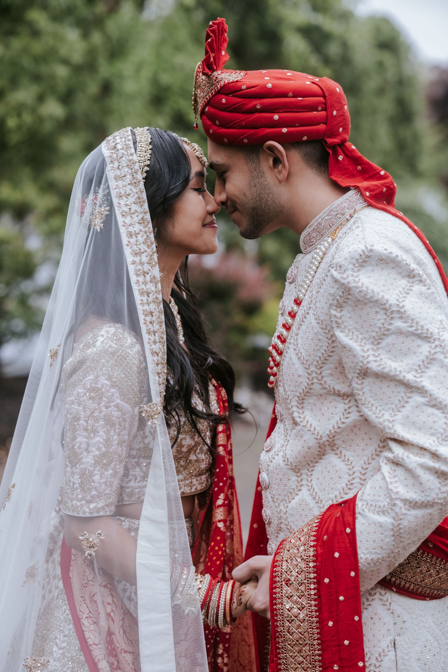 Indian bride and groom sharing a romantic forehead touch moment, dressed in traditional red and white wedding attire.