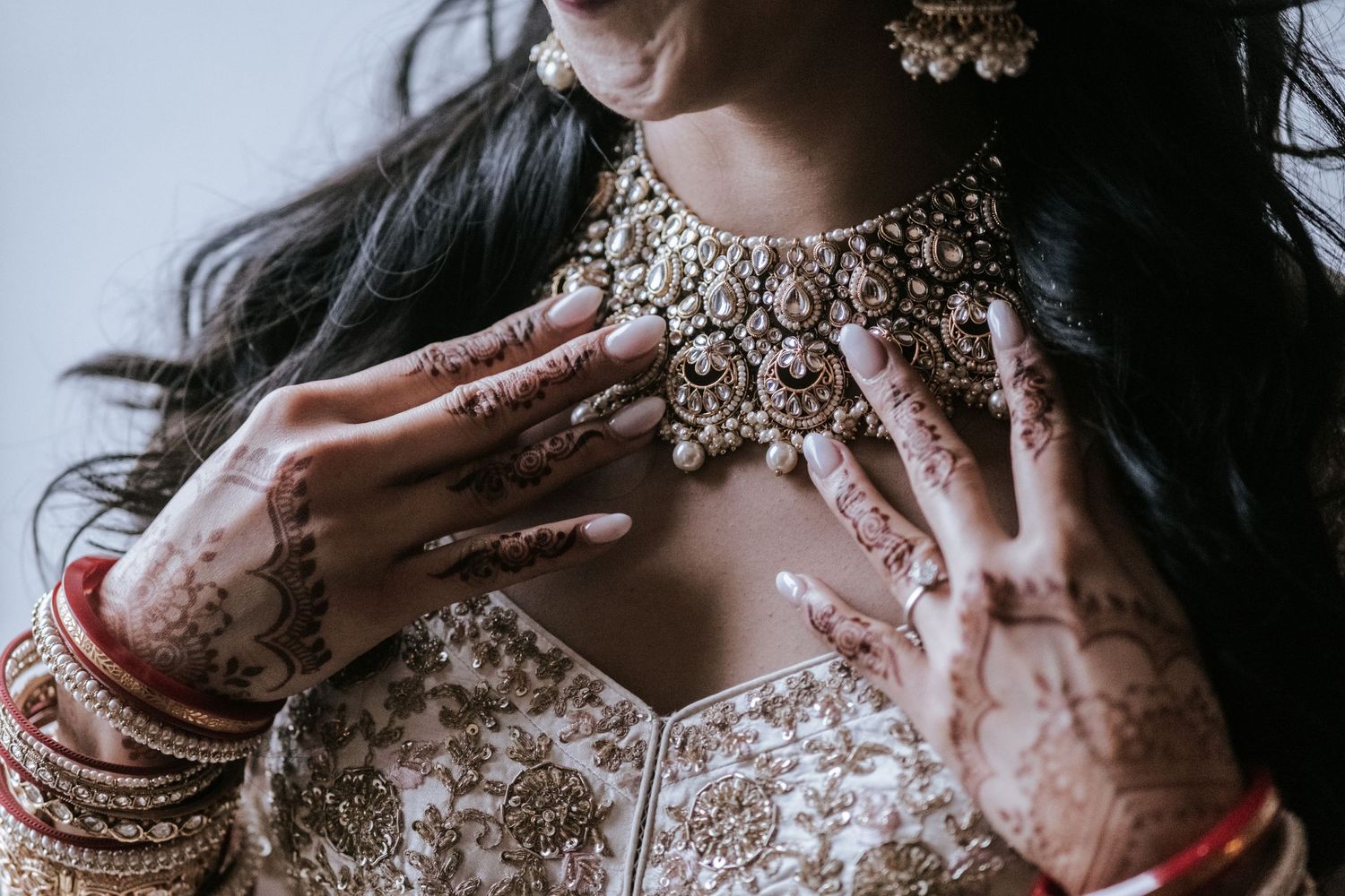 Indian bride adorned with elaborate mehndi, gold kundan necklace, and embroidered white bridal lehenga.