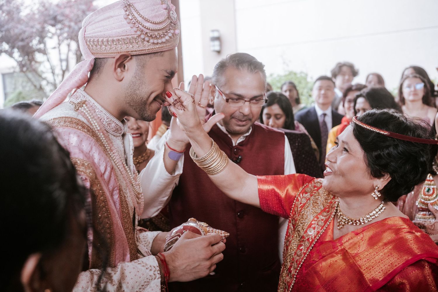 Indian groom in pink sherwani shares a high-five with a woman in red saree at wedding.