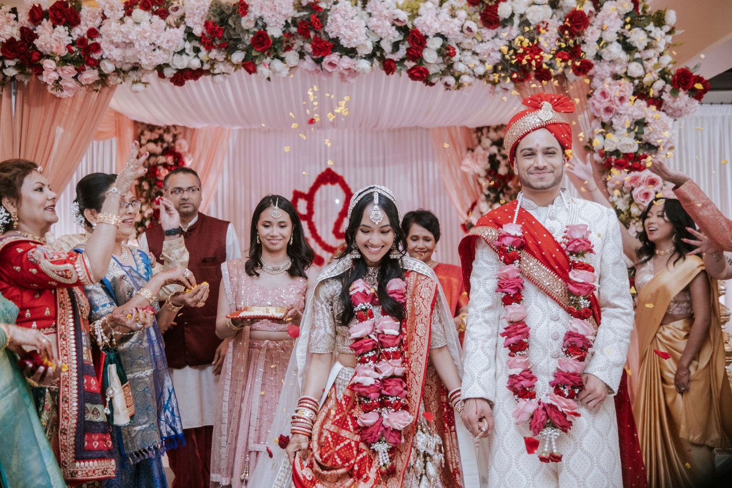 Indian bride and groom walking together after wedding ceremony adorned with red floral garlands and traditional attire.
