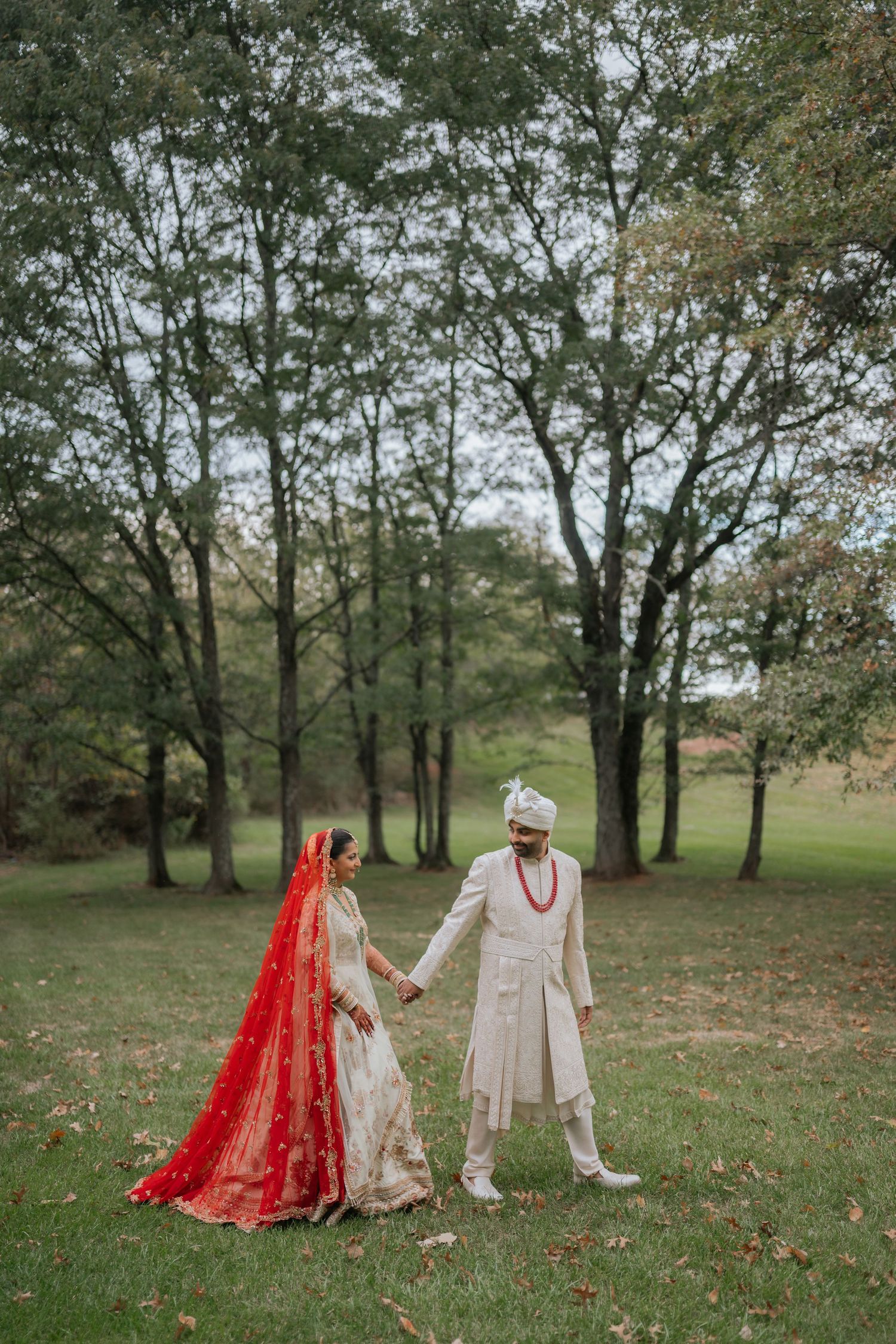 Indian wedding couple in traditional attire holding hands while walking through autumn park.