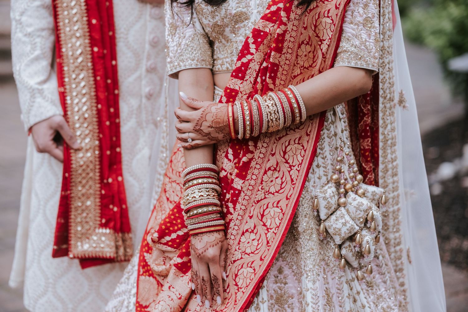Close-up of Indian bride and groom hands with mehndi and gold bangles in wedding attire.