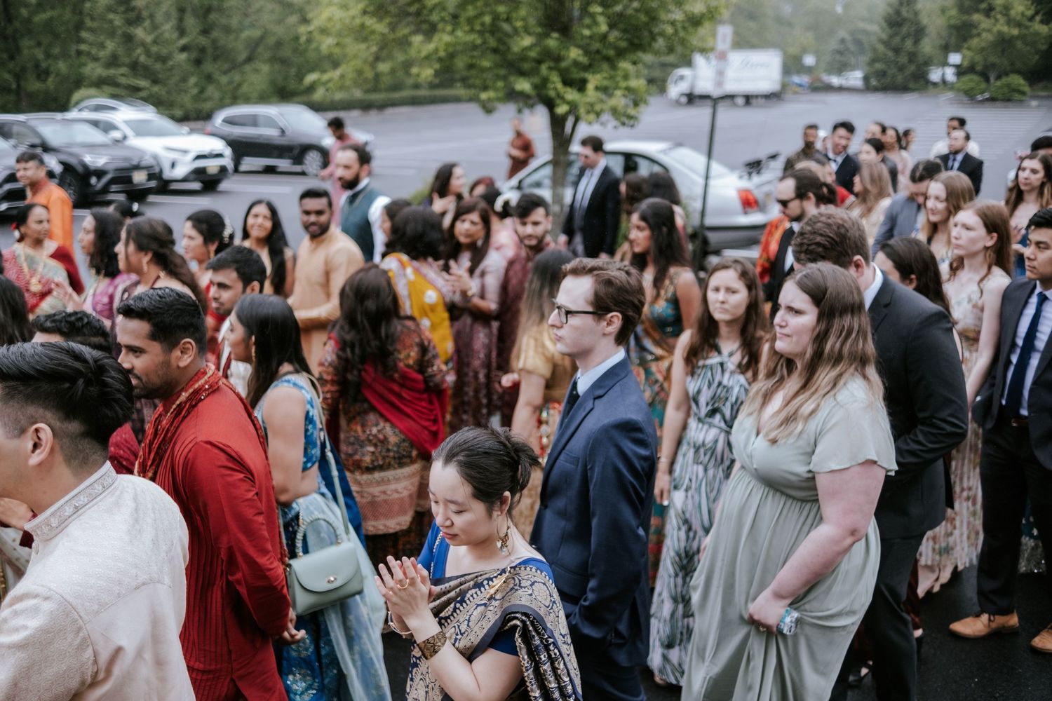 Diverse wedding guests in traditional and formal attire gather outside at an Indian wedding.