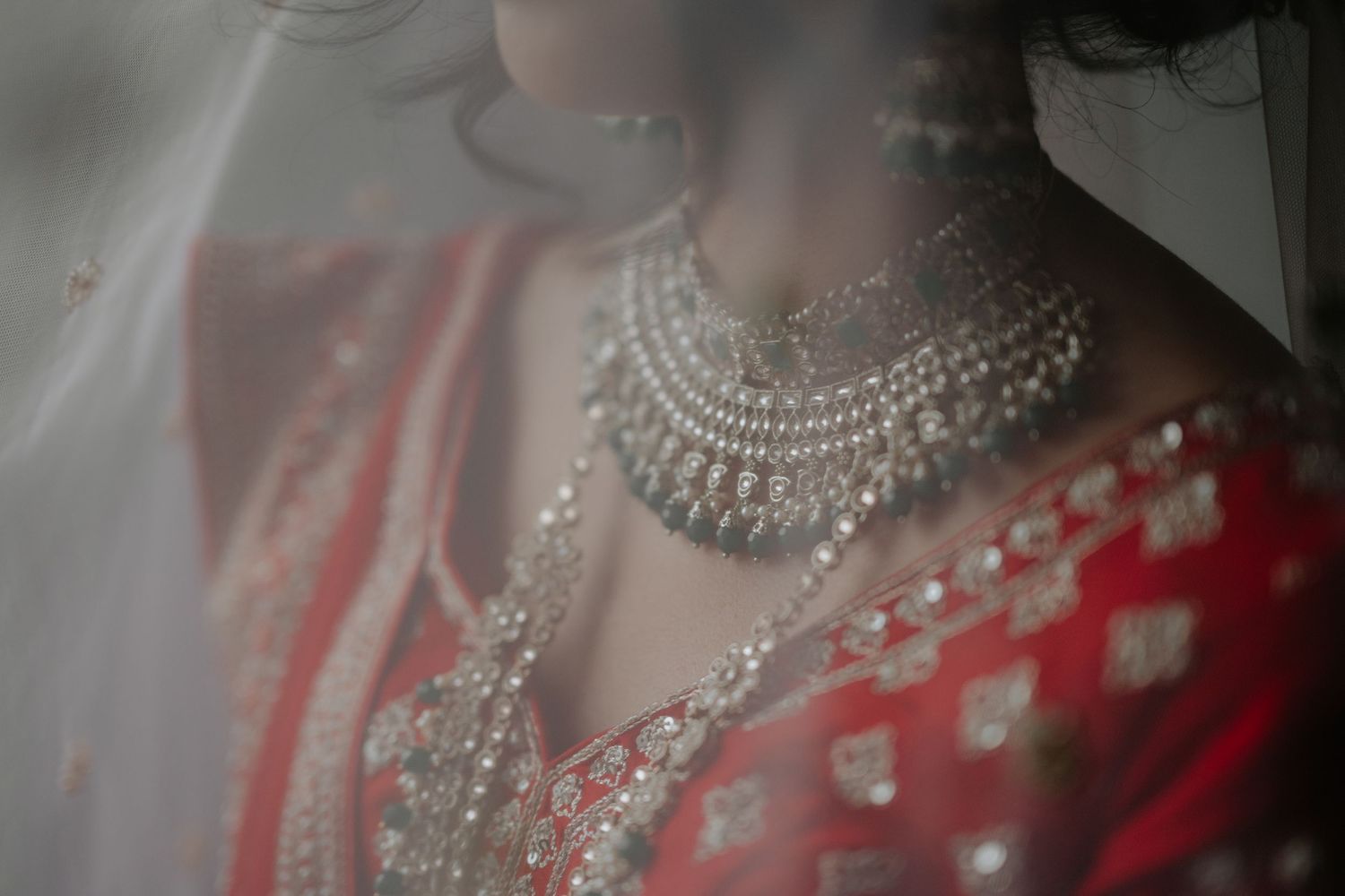 Indian bride in red lehenga wearing elegant silver bridal necklace beneath a sheer veil.