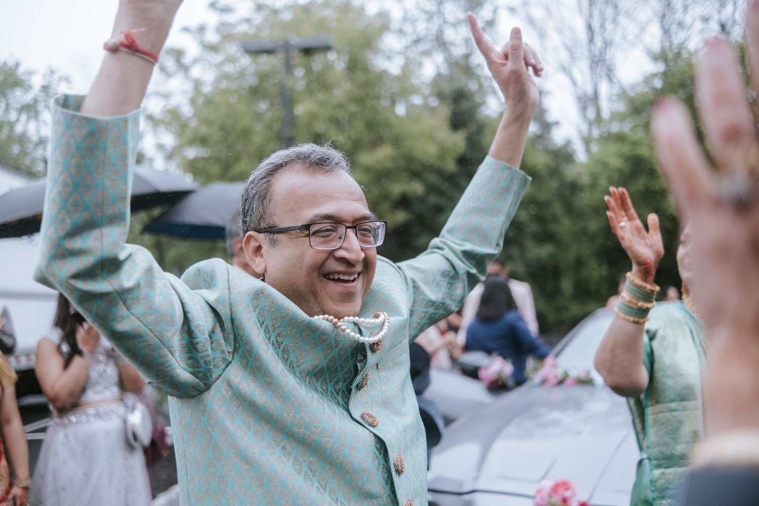 Joyful man in mint green sherwani celebrating with hands raised at an Indian wedding baraat.
