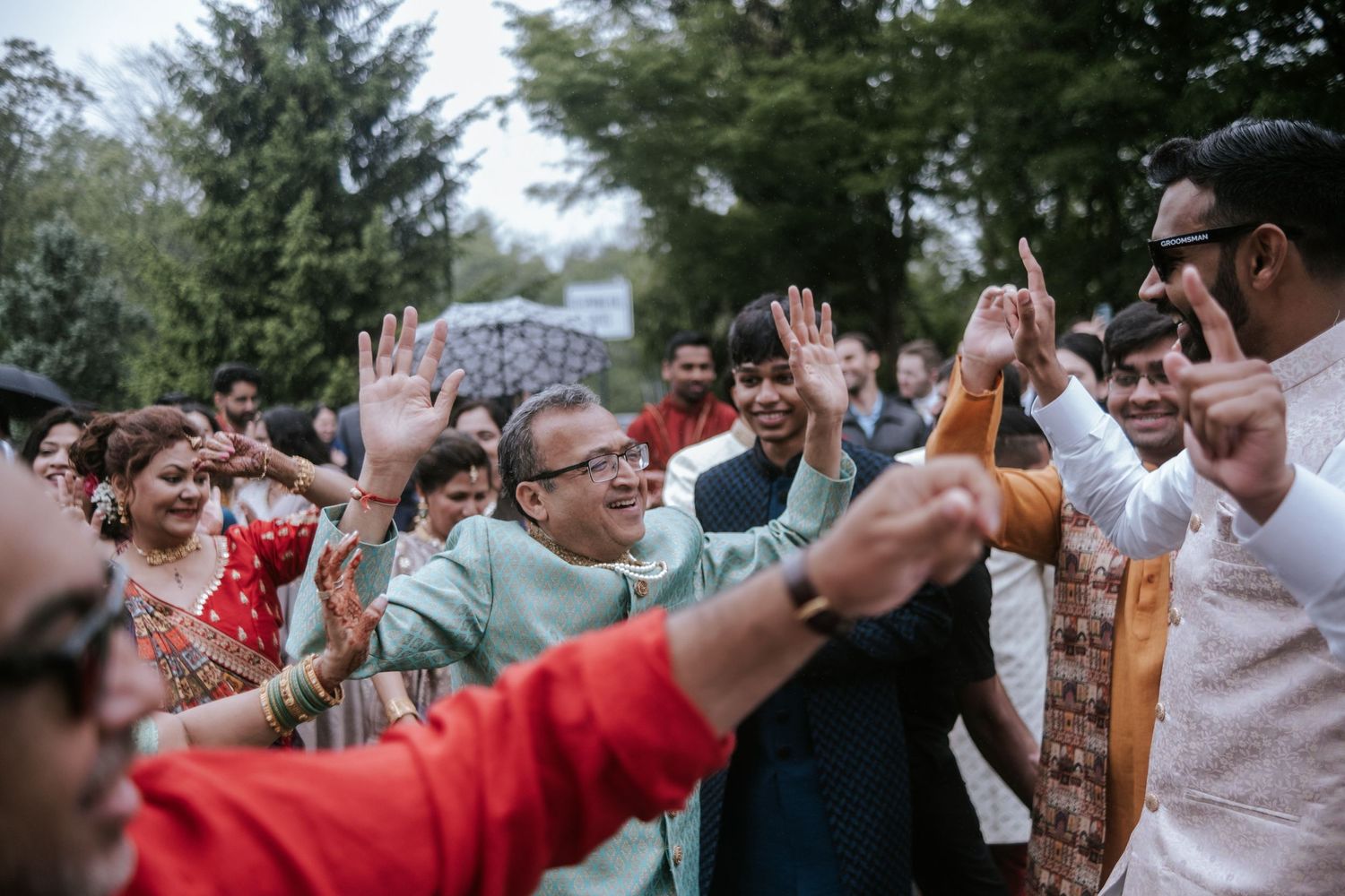 Guests in colorful Indian attire dancing and celebrating during a lively outdoor wedding baraat.