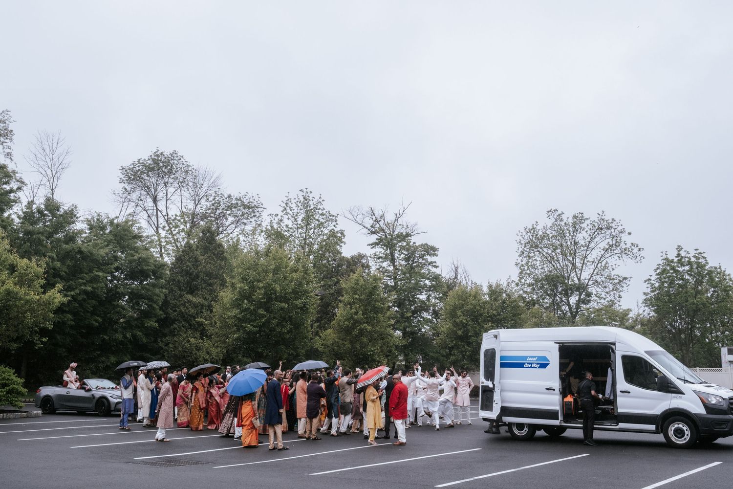 Large Indian wedding baraat procession gathering in a parking lot on a cloudy day.
