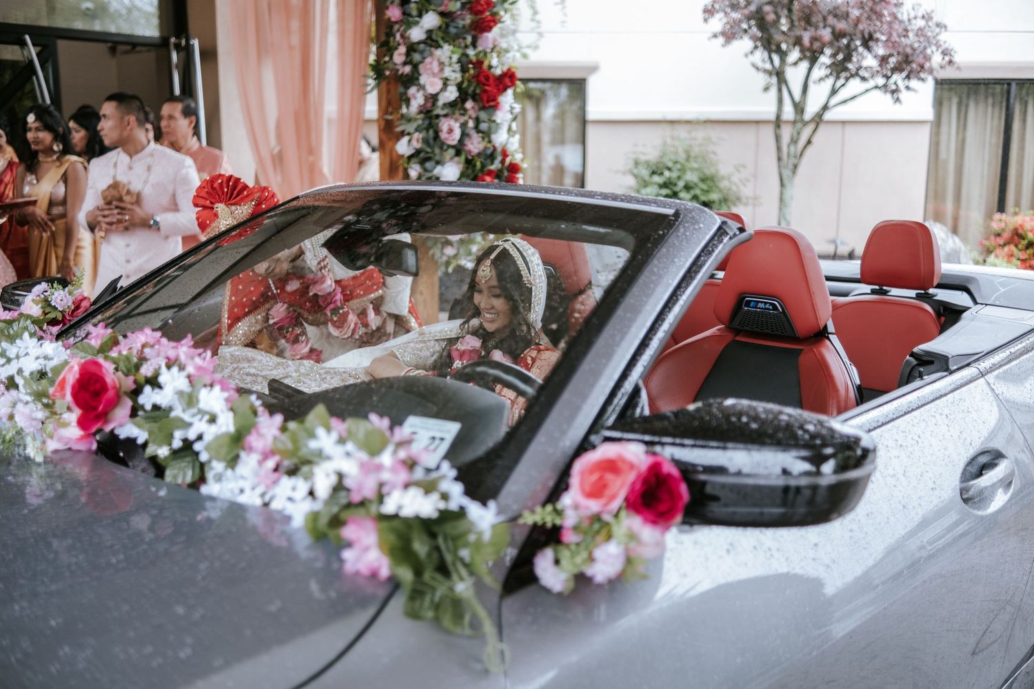 Bride and groom seated in a flower-decorated convertible car during Indian wedding send-off celebration.