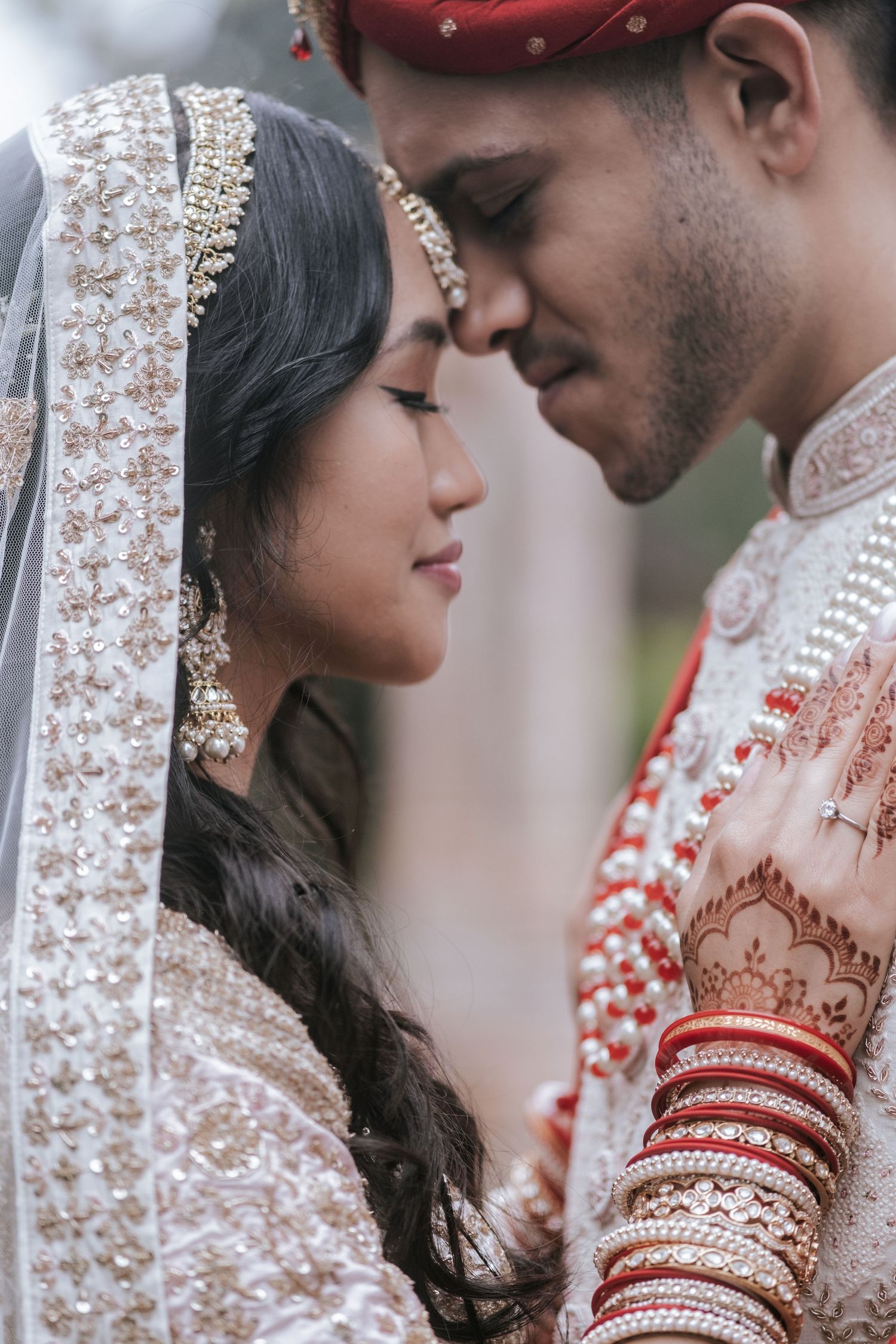 Indian bride and groom in traditional bridal attire share a romantic nose-to-nose moment during wedding portrait.