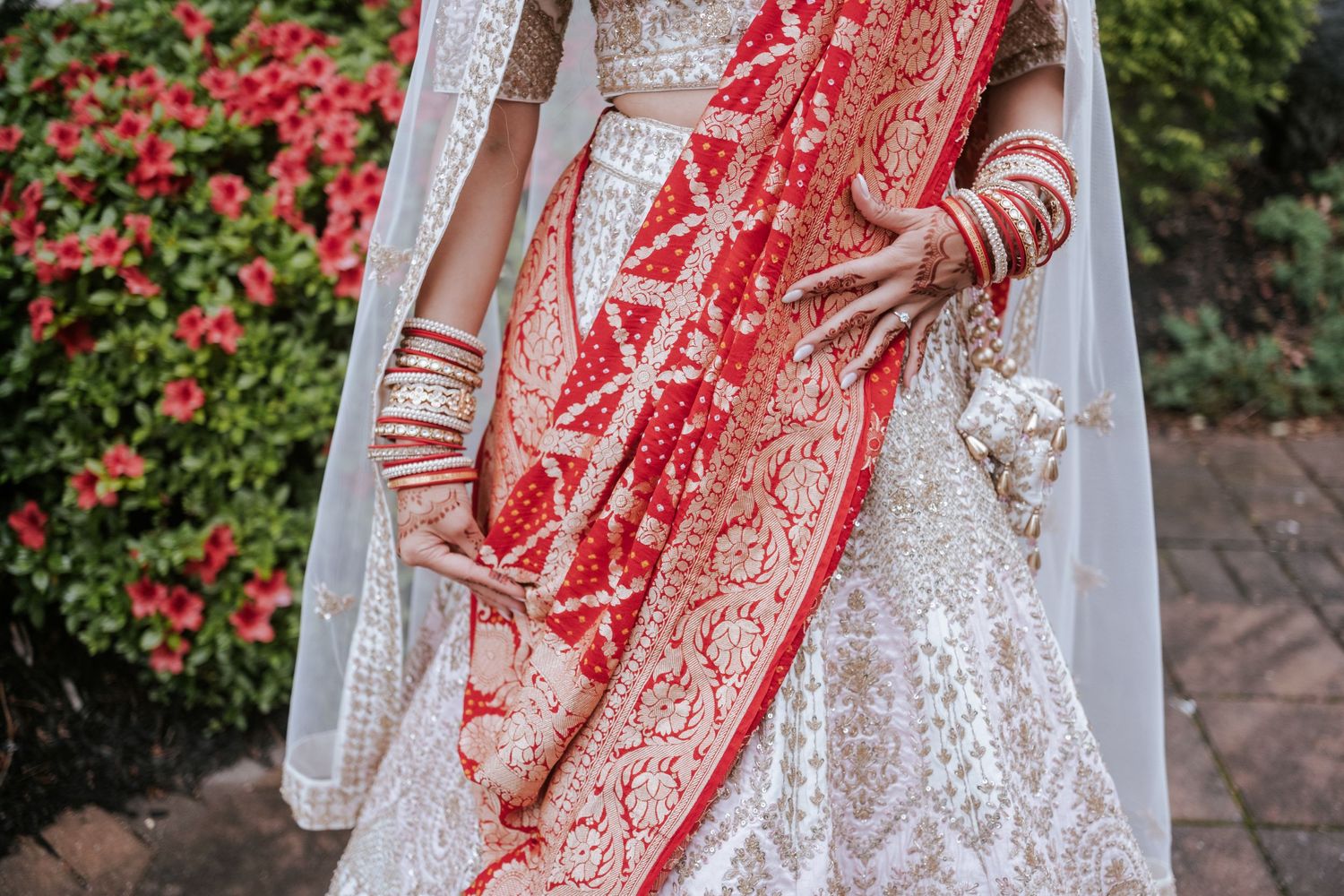 Close-up of Indian bride in embroidered white lehenga with red dupatta and gold bangles.