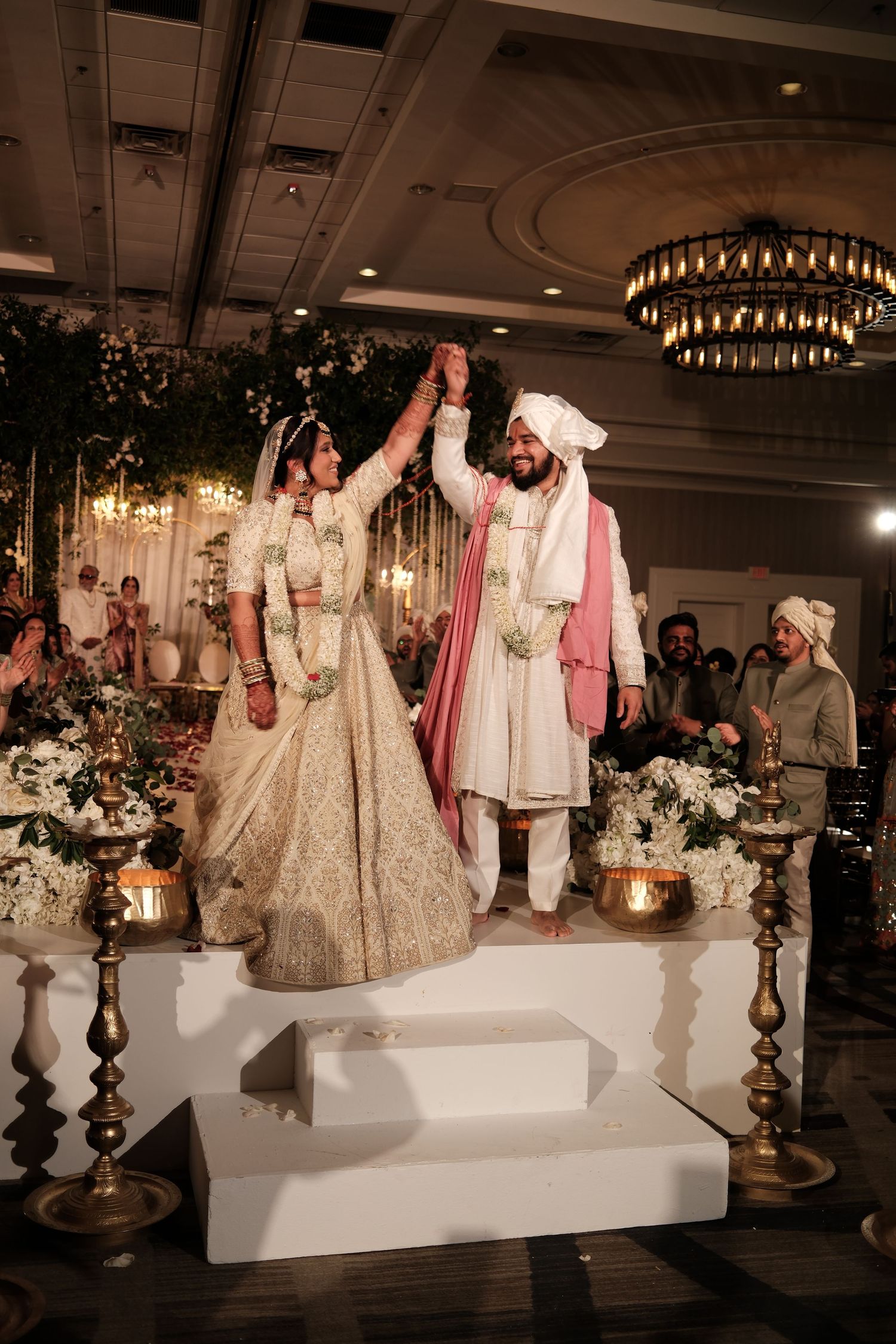 Indian bride and groom hold hands raised on stage during traditional Sikh wedding ceremony indoors.