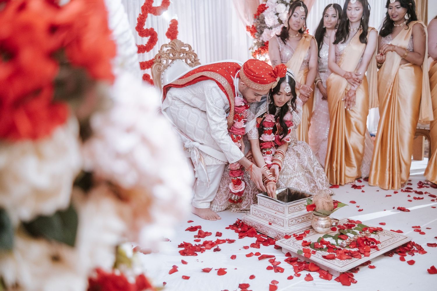 Indian groom and bride performing traditional Hindu wedding ritual with rose petals scattered on the floor.