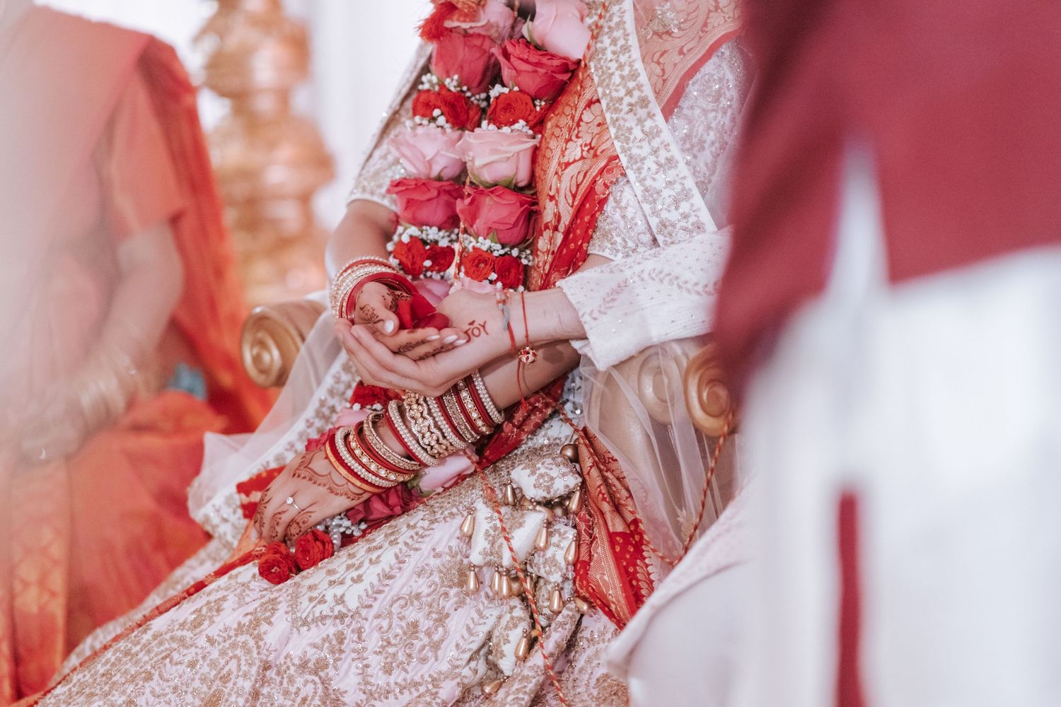 Close-up of Indian bride's hands adorned with mehndi and red bangles in bridal lehenga.