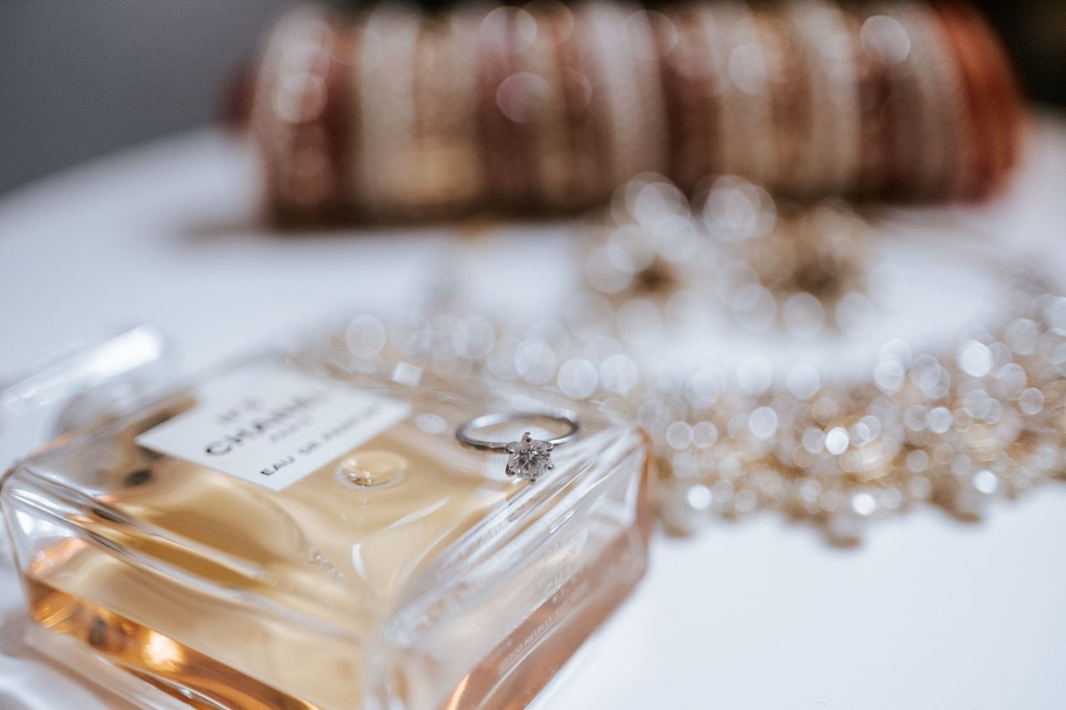 Diamond engagement ring rests on perfume bottle with bridal bangles and jewelry nearby.