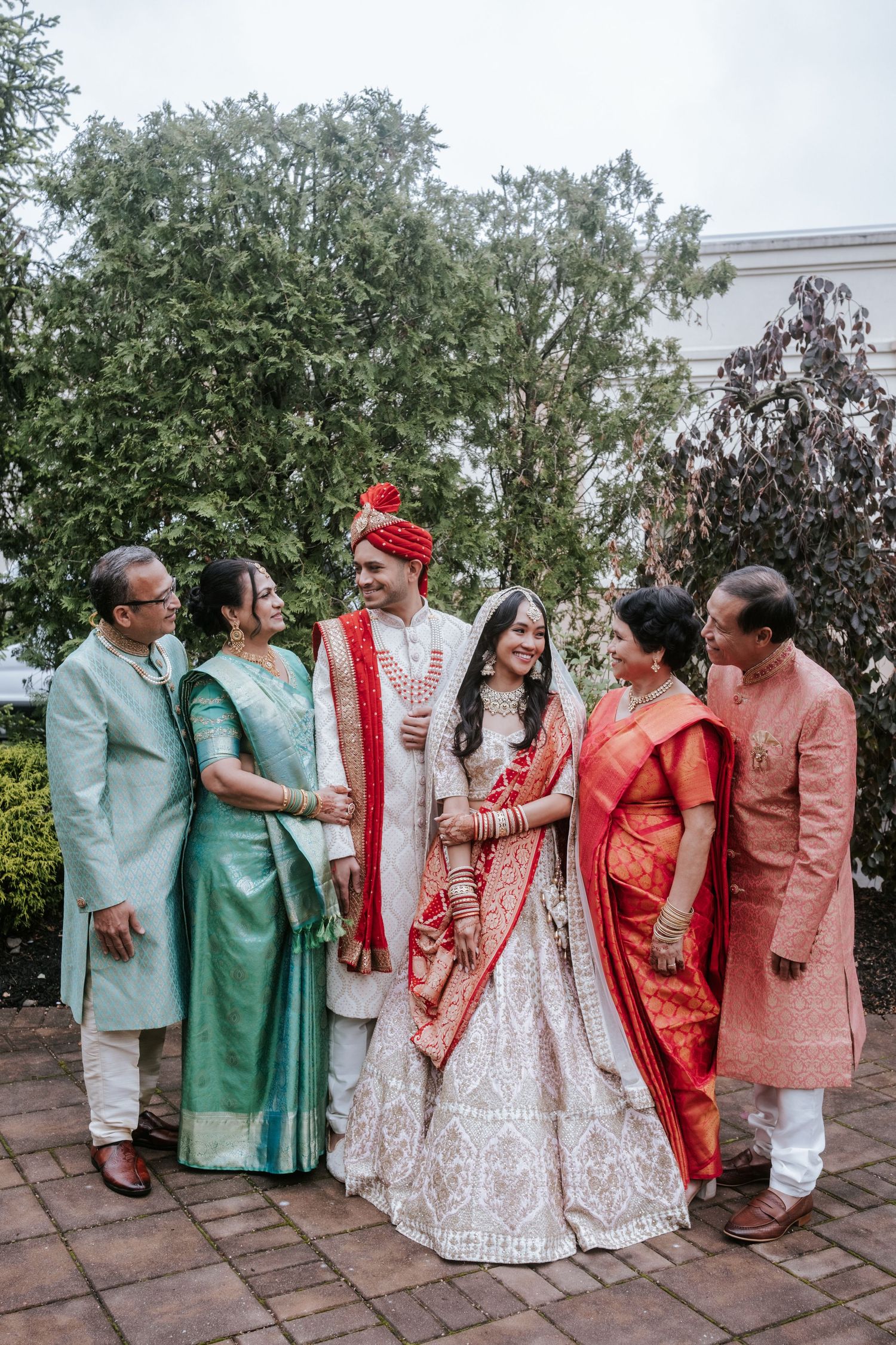 Indian bride and groom with both families posing together outdoors, wearing traditional Indian wedding attire.