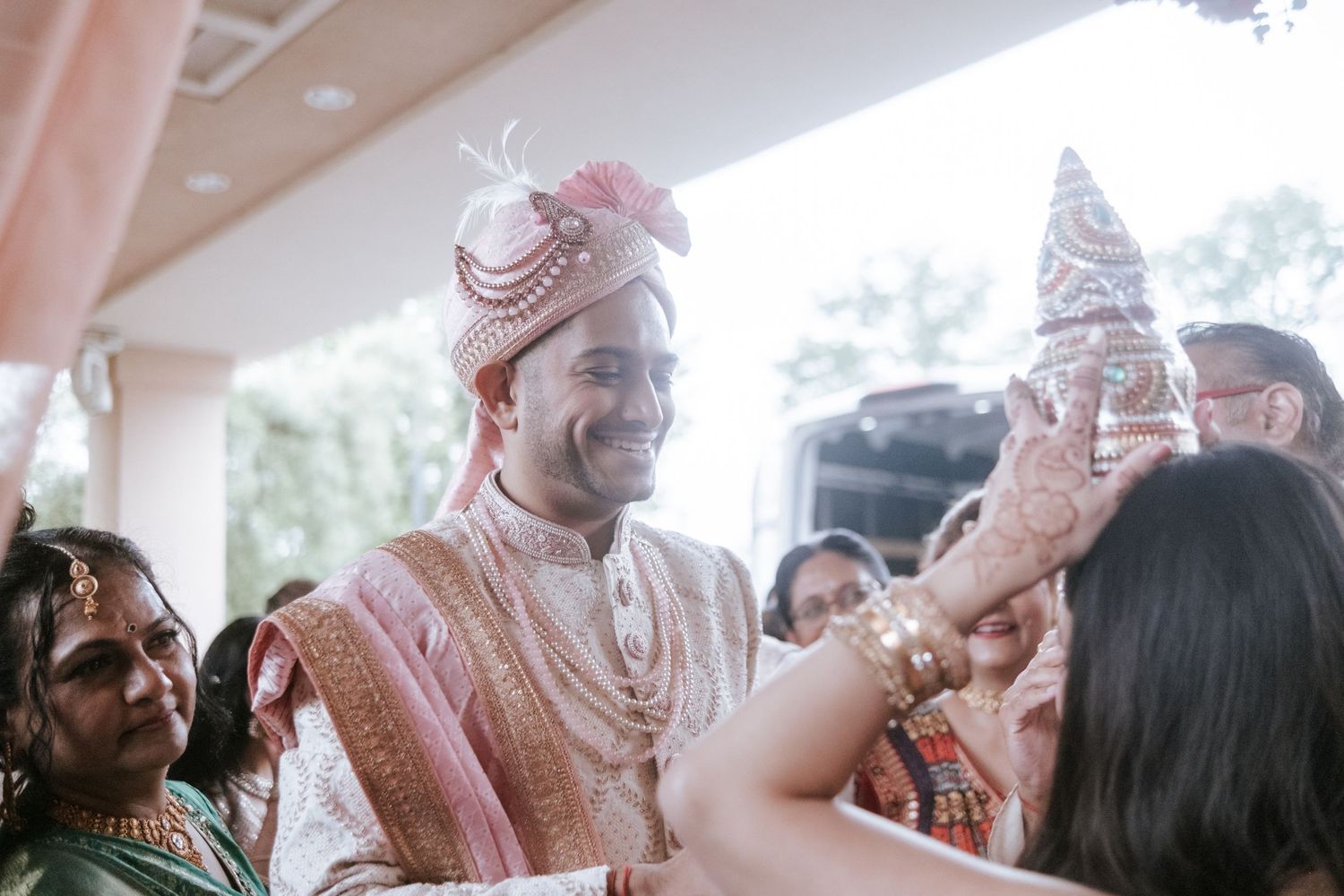 Indian groom in pink sherwani and turban smiles during traditional Hindu wedding ceremony ritual.