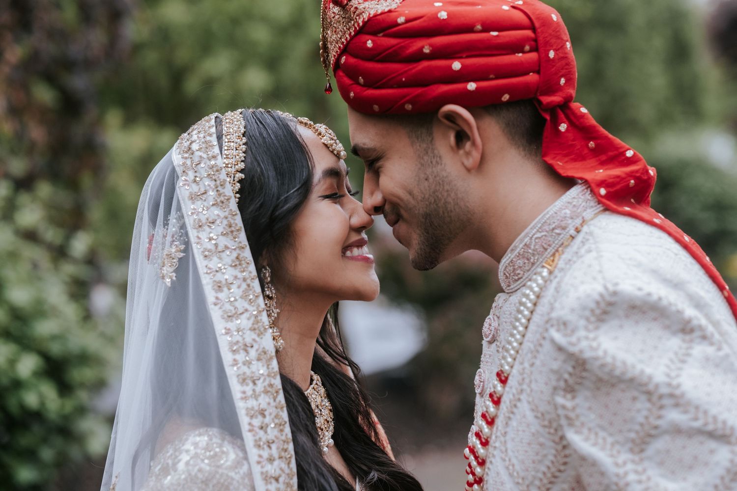 Indian bride and groom in traditional wedding attire sharing romantic moment outdoors.