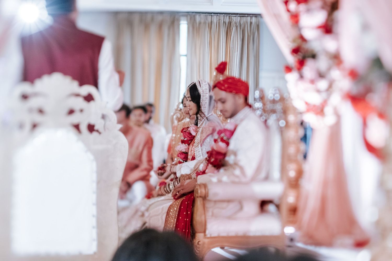 Bride and groom seated together during a traditional Indian wedding ceremony with red floral decorations.